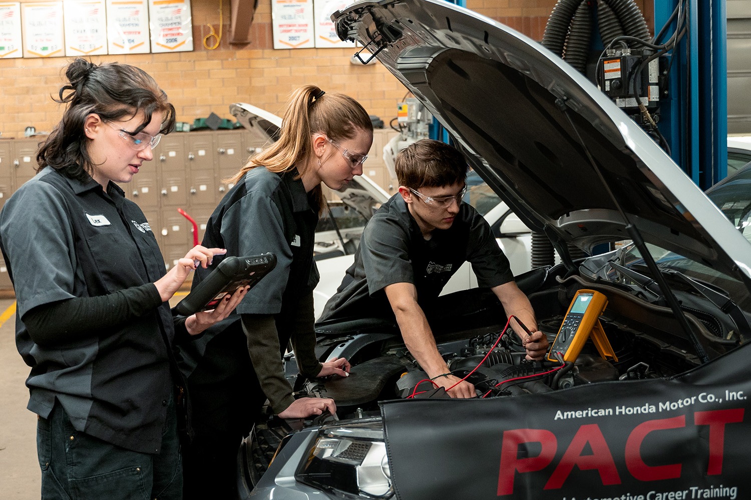 2 STUDENTS WORKING UNDER A HOOD OF CAR