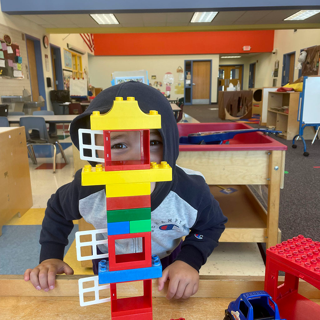 Preschool student looking through the top of a tower he built with LEGOS