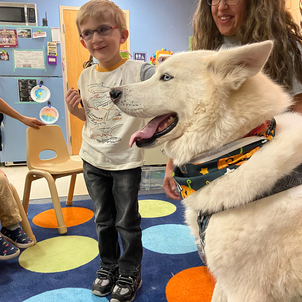 Preschool student with a white dog who is visiting the classroom