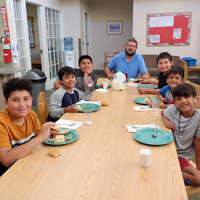 Students and a staff member at long table eating dinner in the cottages