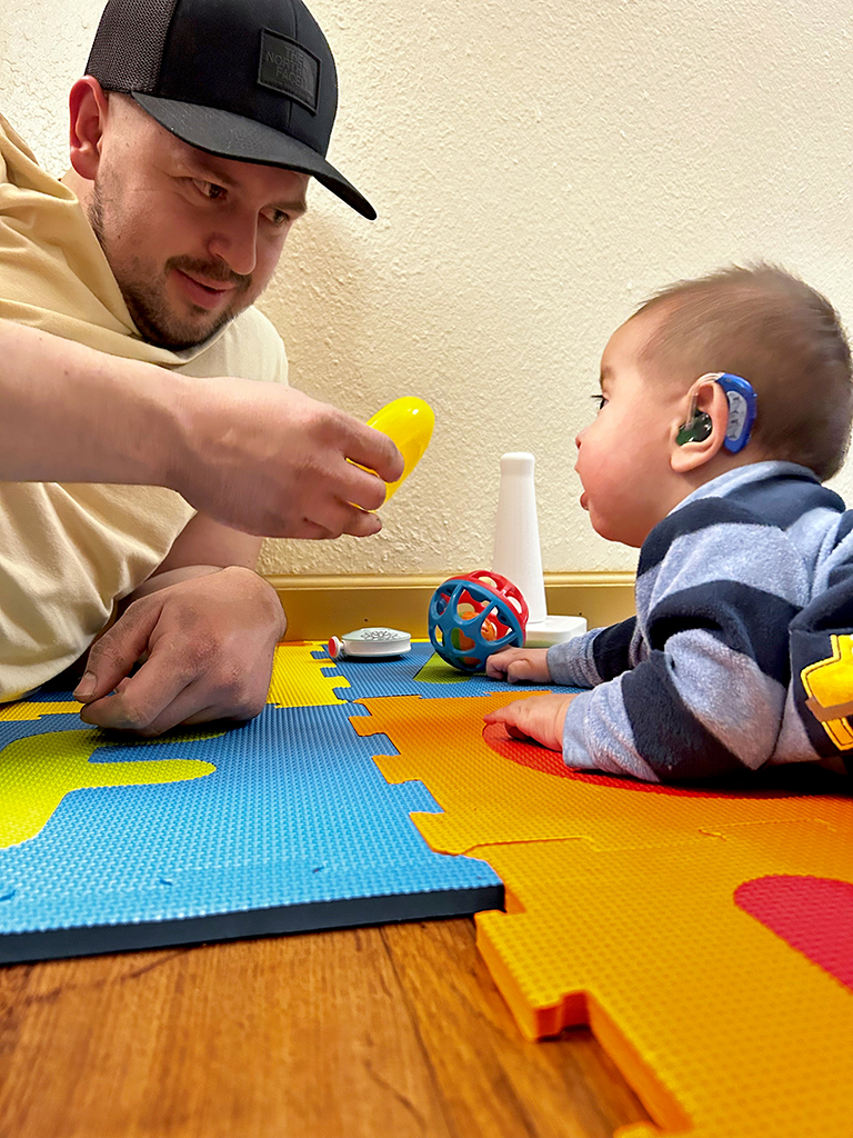 Father playing with baby on  floor during home visit  from Early Intervention and Developmental Services