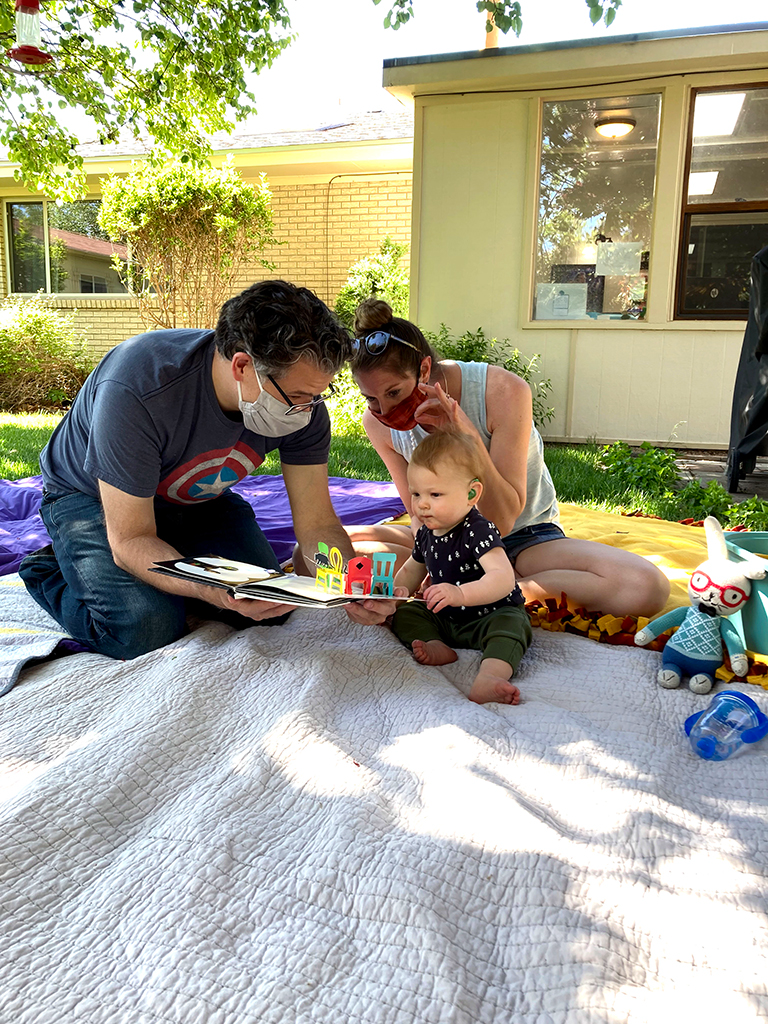 Parents and baby reading a pop-up book on a blanket outside during home visit  from Early Intervention Developmental Services