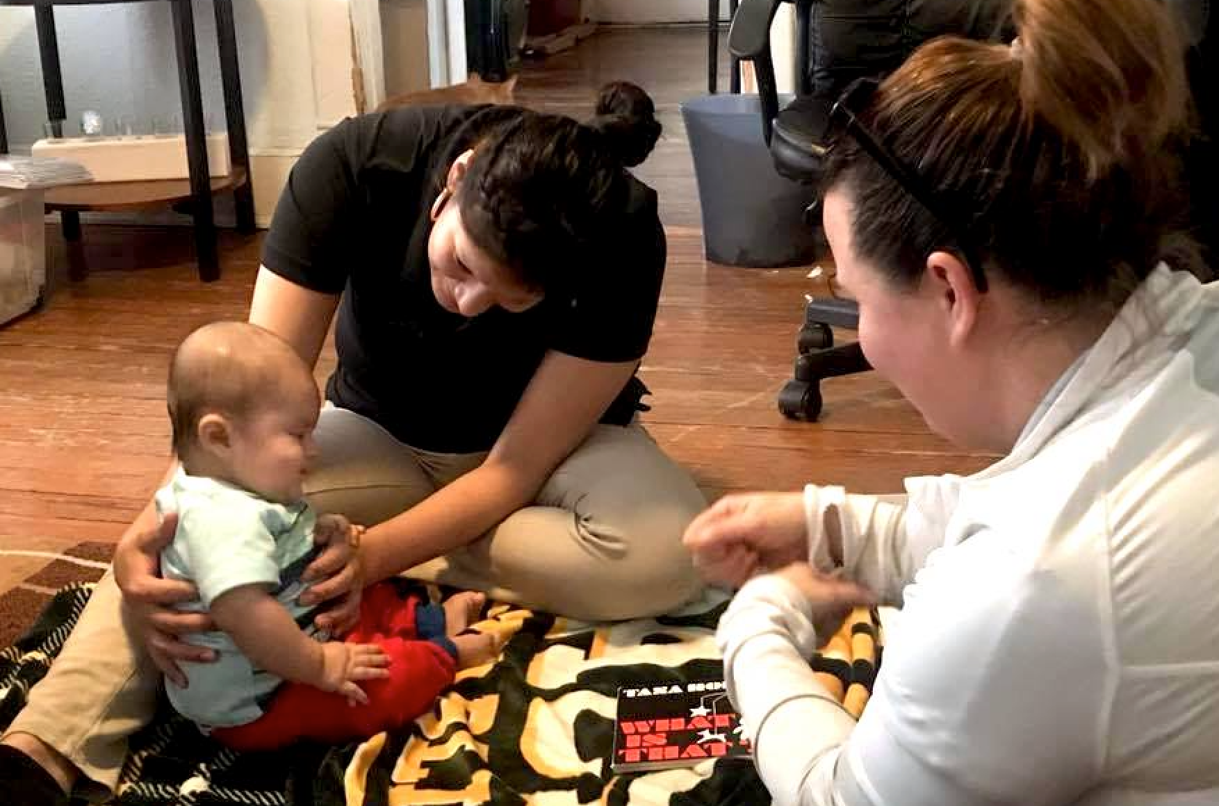 Mother sitting on the floor of her apartment with her young baby, and a social worker also on the floor.