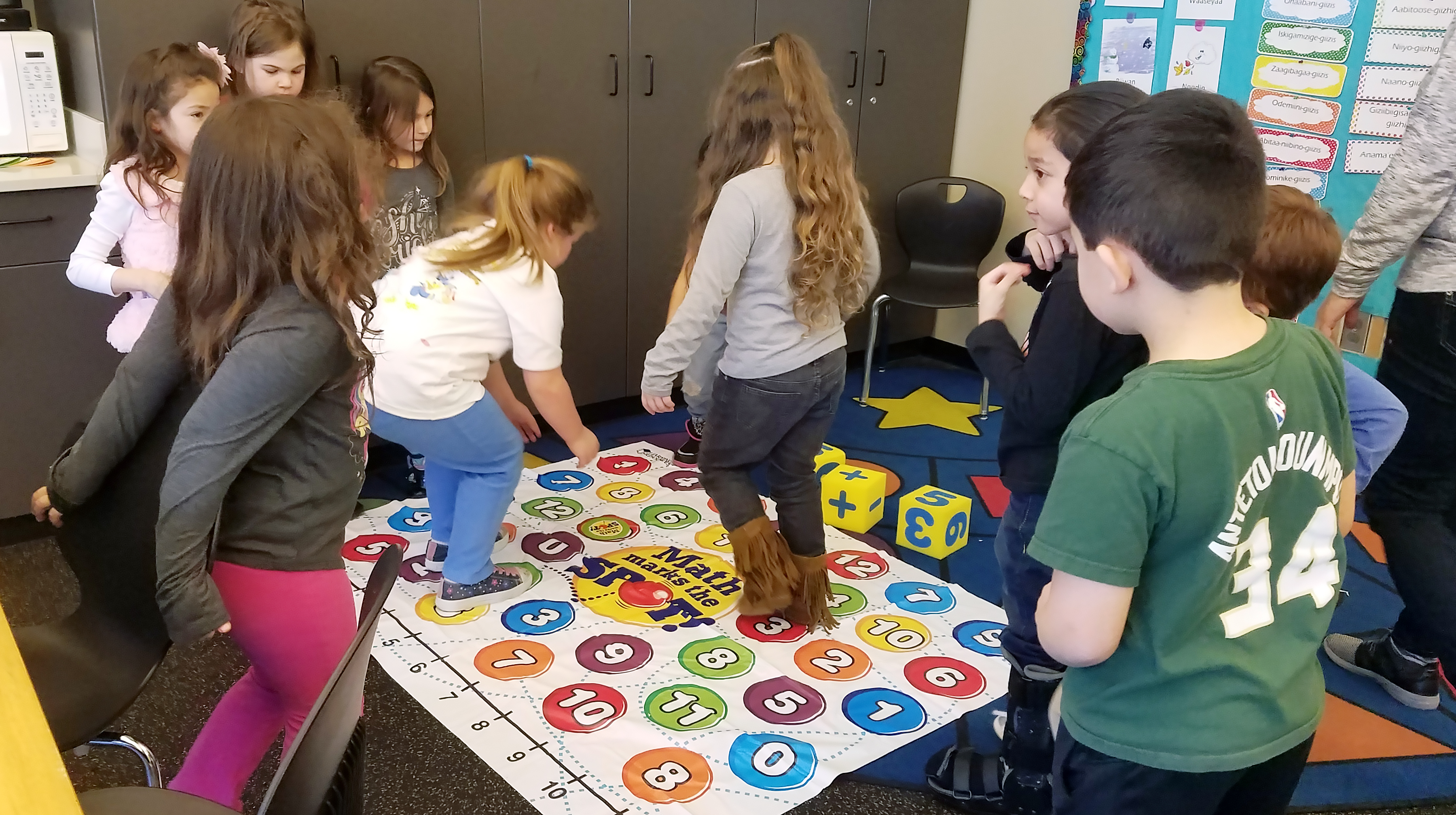 Nine students playing a game with numbers on the floor. They are stopping on the numbers.