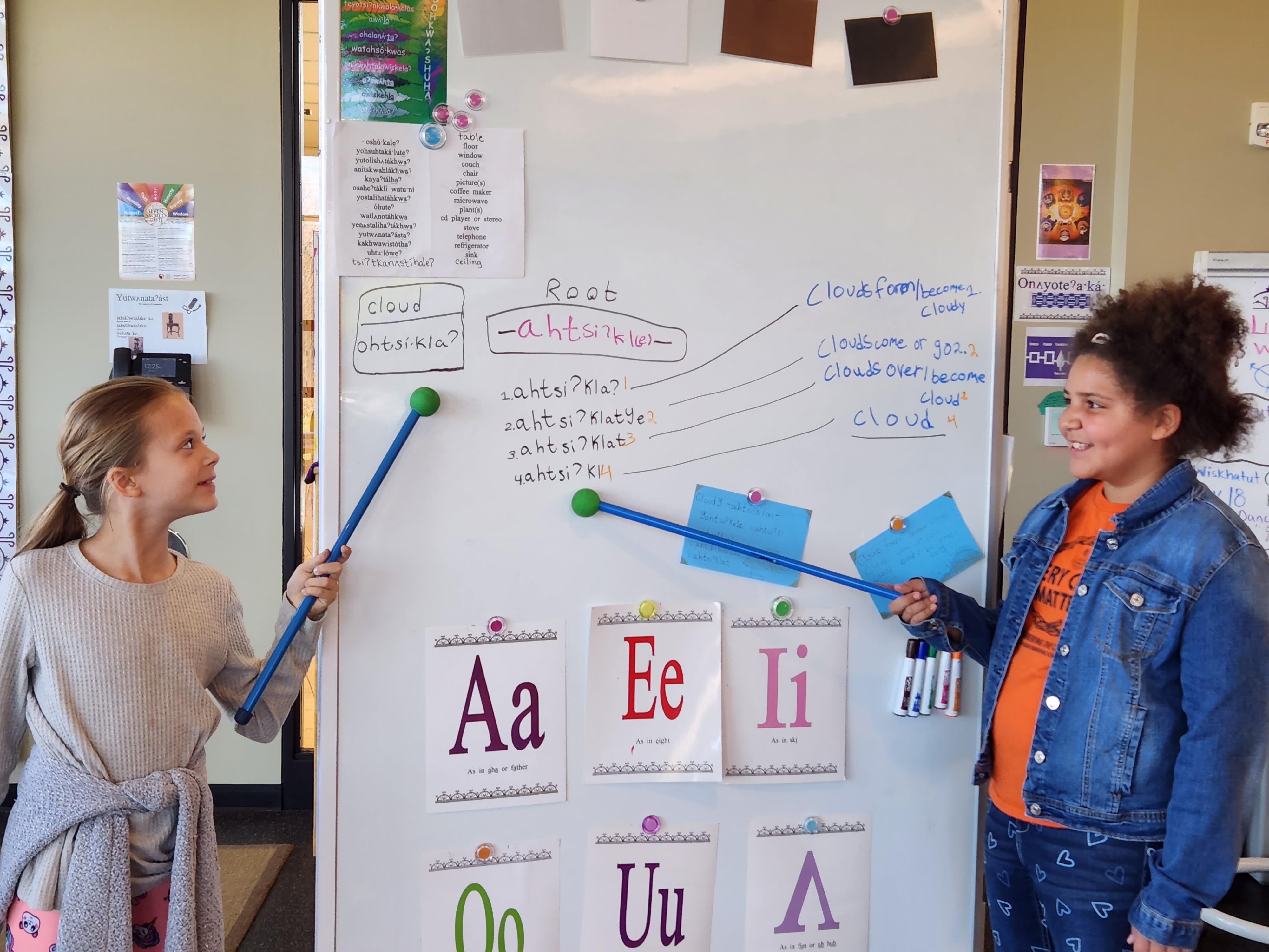 Two Oneida students pointing at Oneida words on a dry erase board.