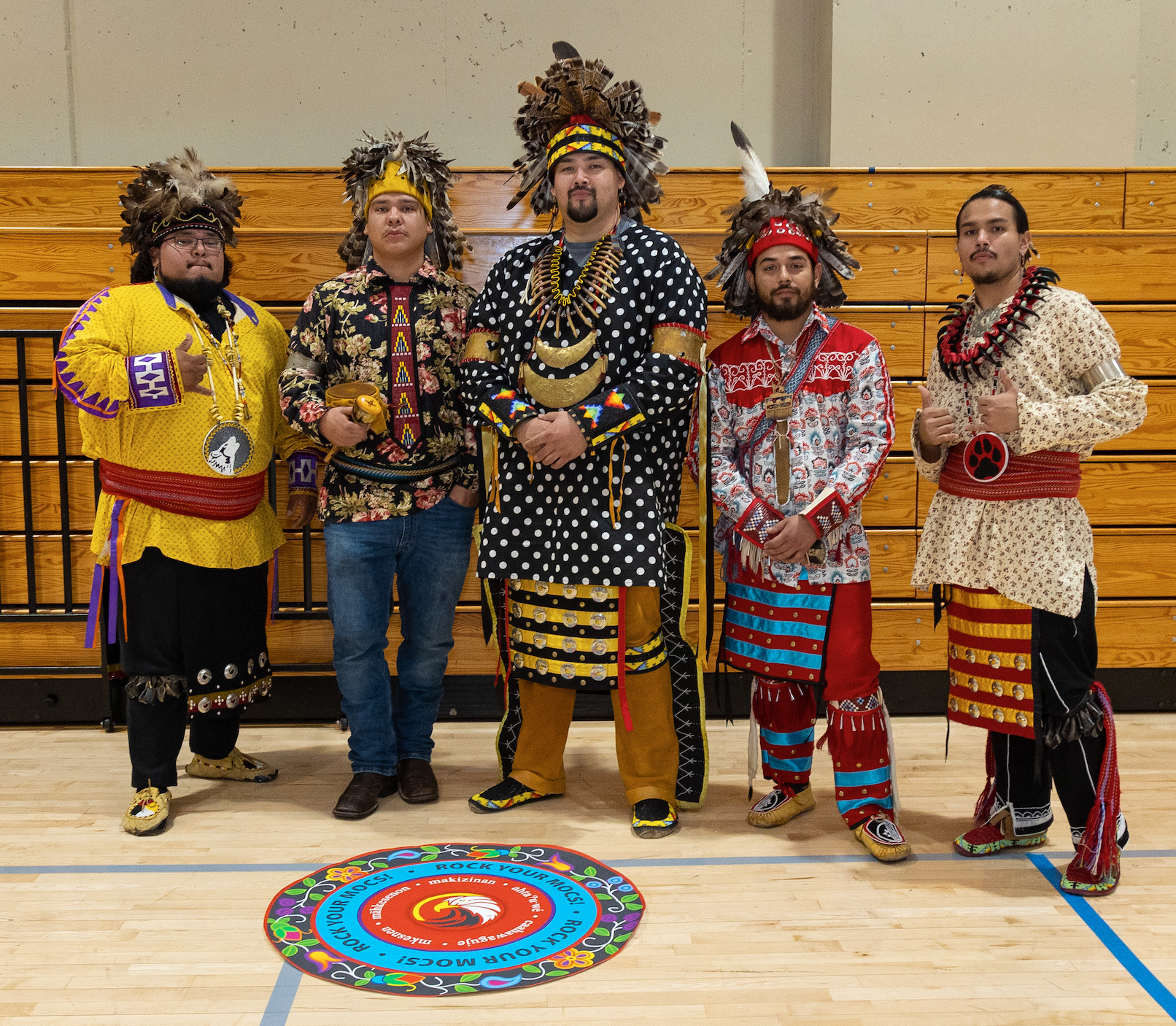 Five Oneida men called the Longhouse Singers standing inside the gym wearing  regalia.