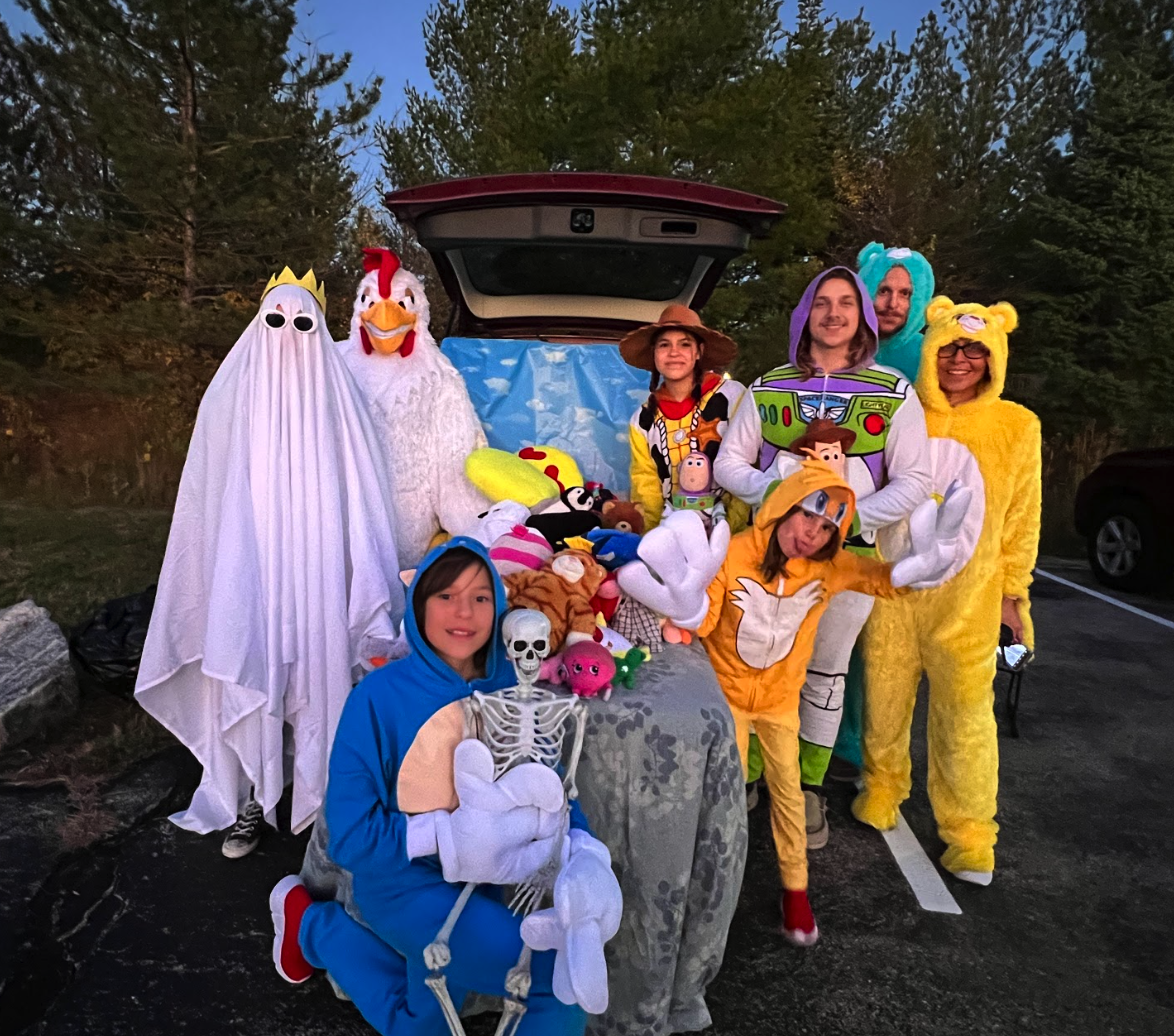 A mix of adults and children dressed up in costumes outside of car trunk that has been decorated for Trunk or Treat.