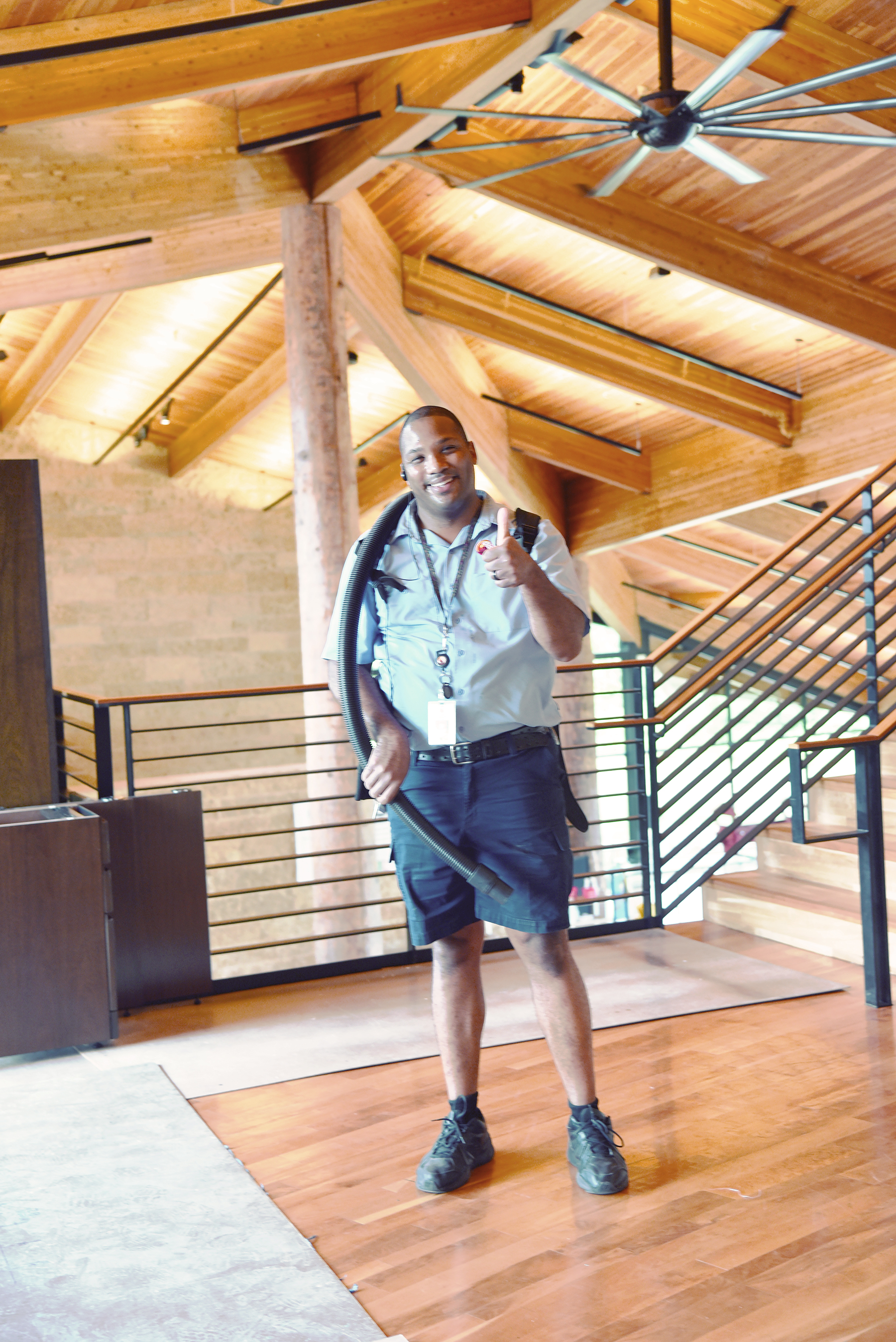 Cleaner staff member, smiling, thumbs up, holding vacuum inside the school.