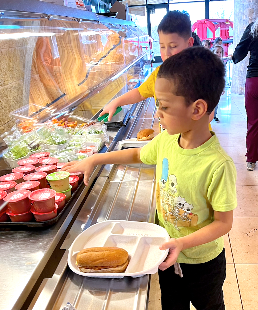 Two young boys coming through the food service line, choosing their food items.