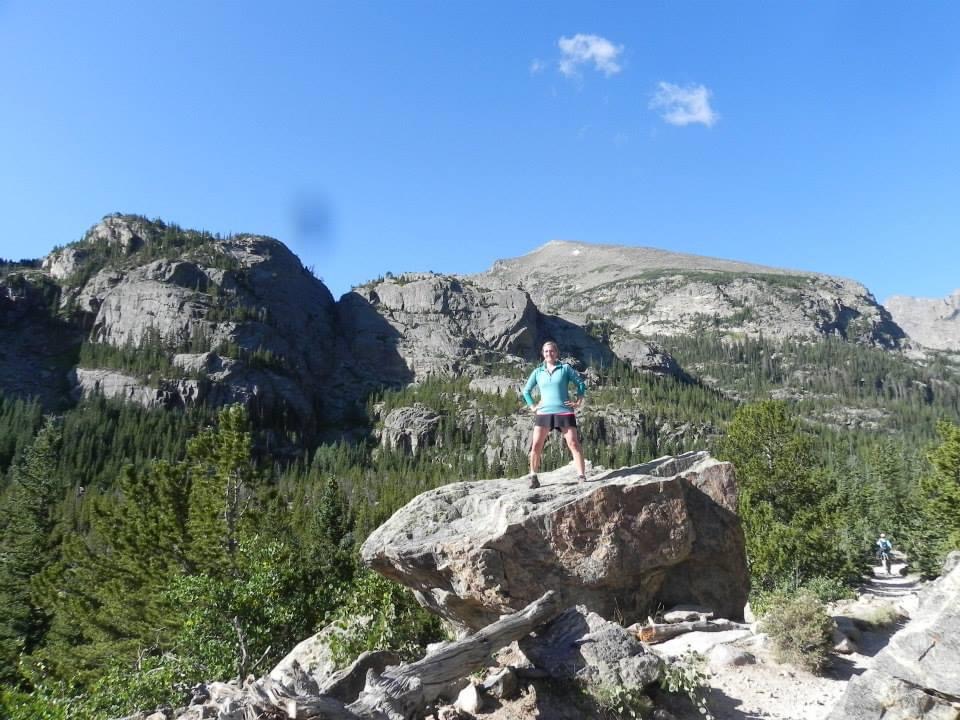 Woman standing on rock formation on mountain. Blue sky background.