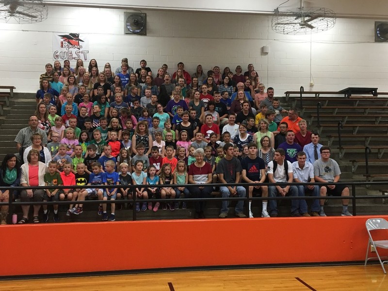 A photo of students and teachers in the gym on the bleachers