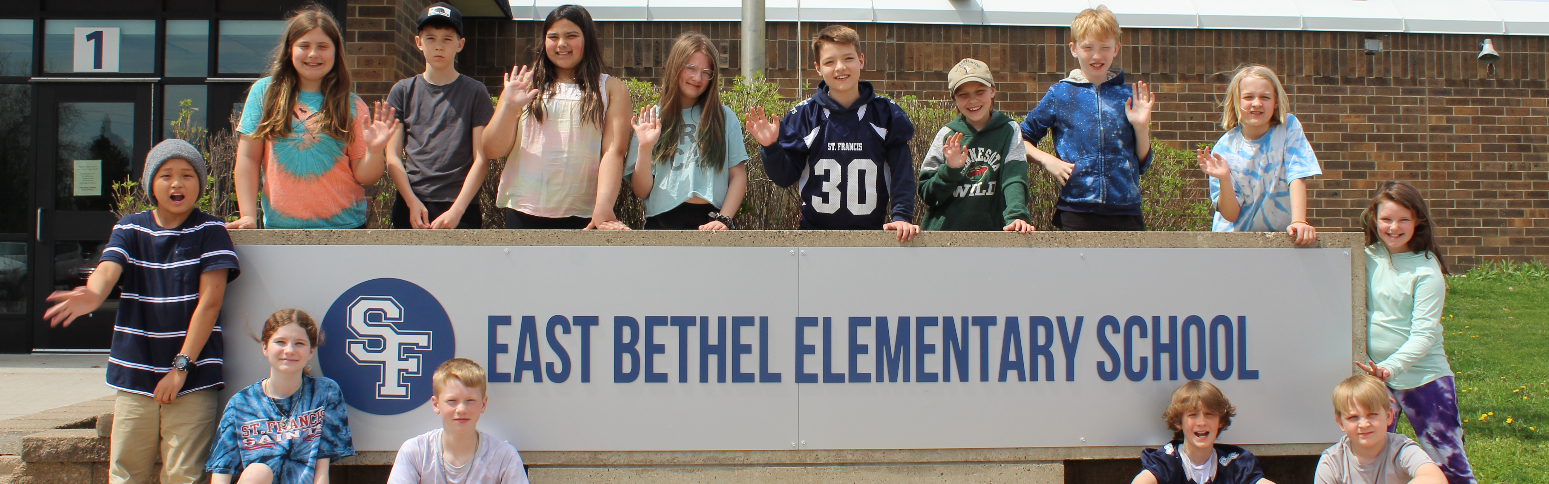 Image: Students waving and standing around the East Bethel Elementary School Sign