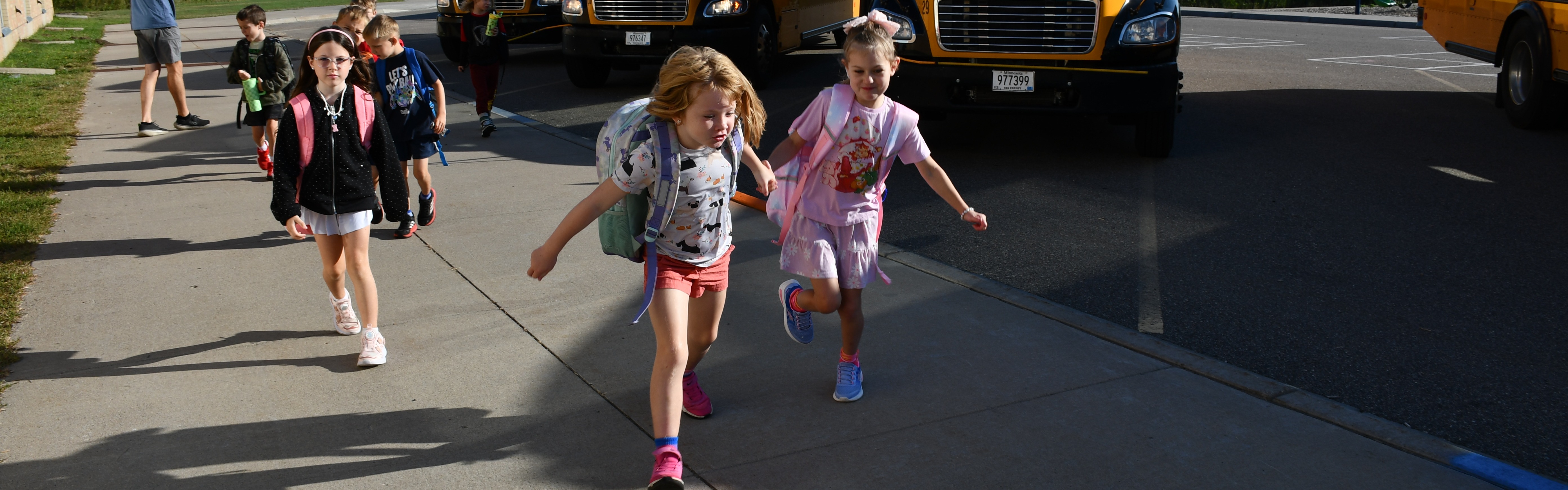 girls running on sidewalk with bus in background