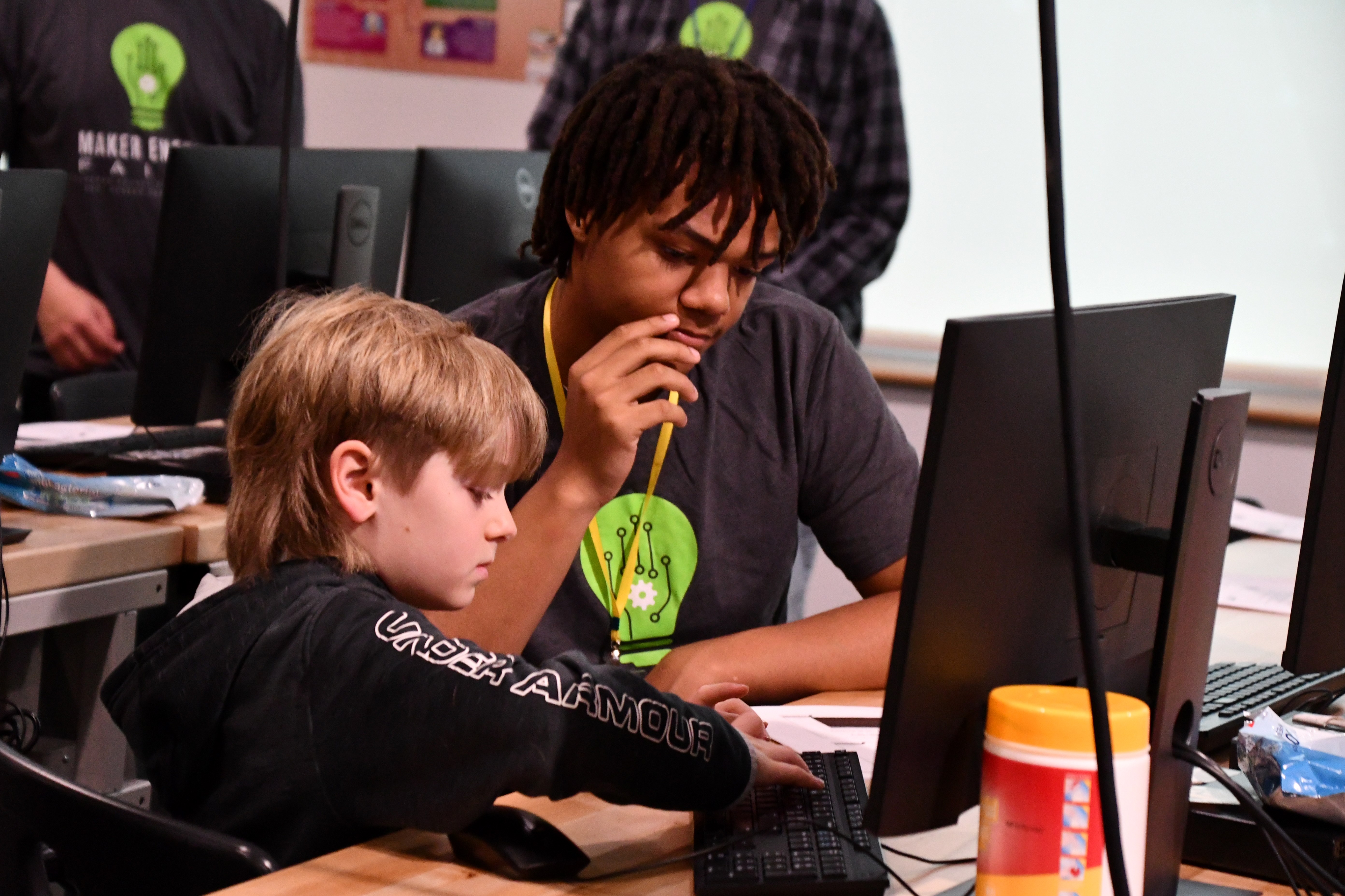 older student helping younger student code on a computer