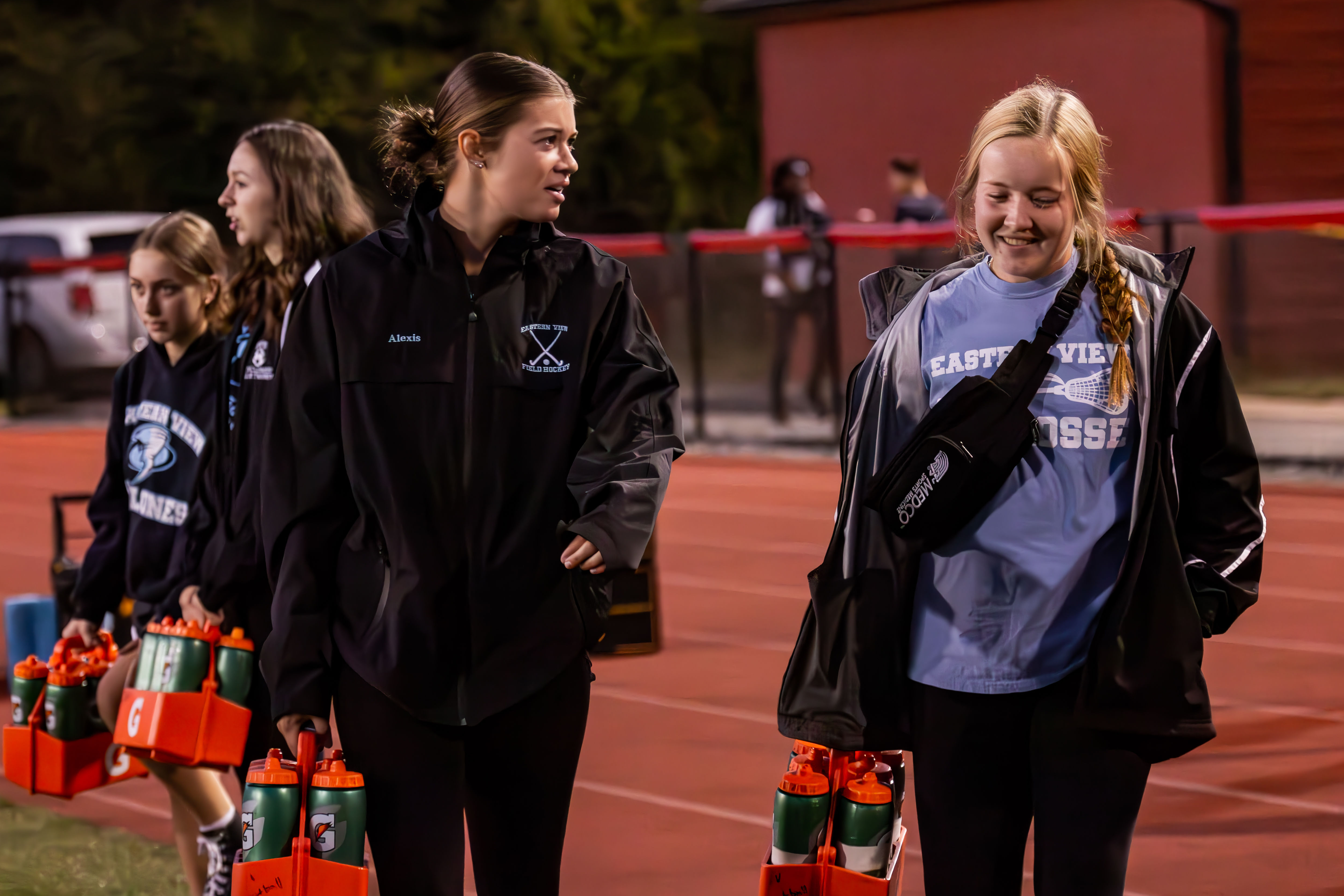 student athletic trainers carrying water bottles on the track 