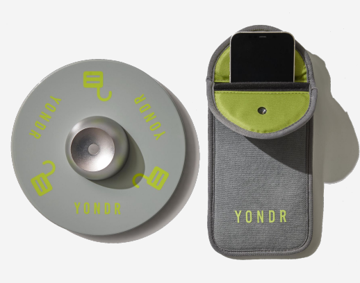 round gray Yondr base unit next to a gray Yondr pouch with a cell phone in it