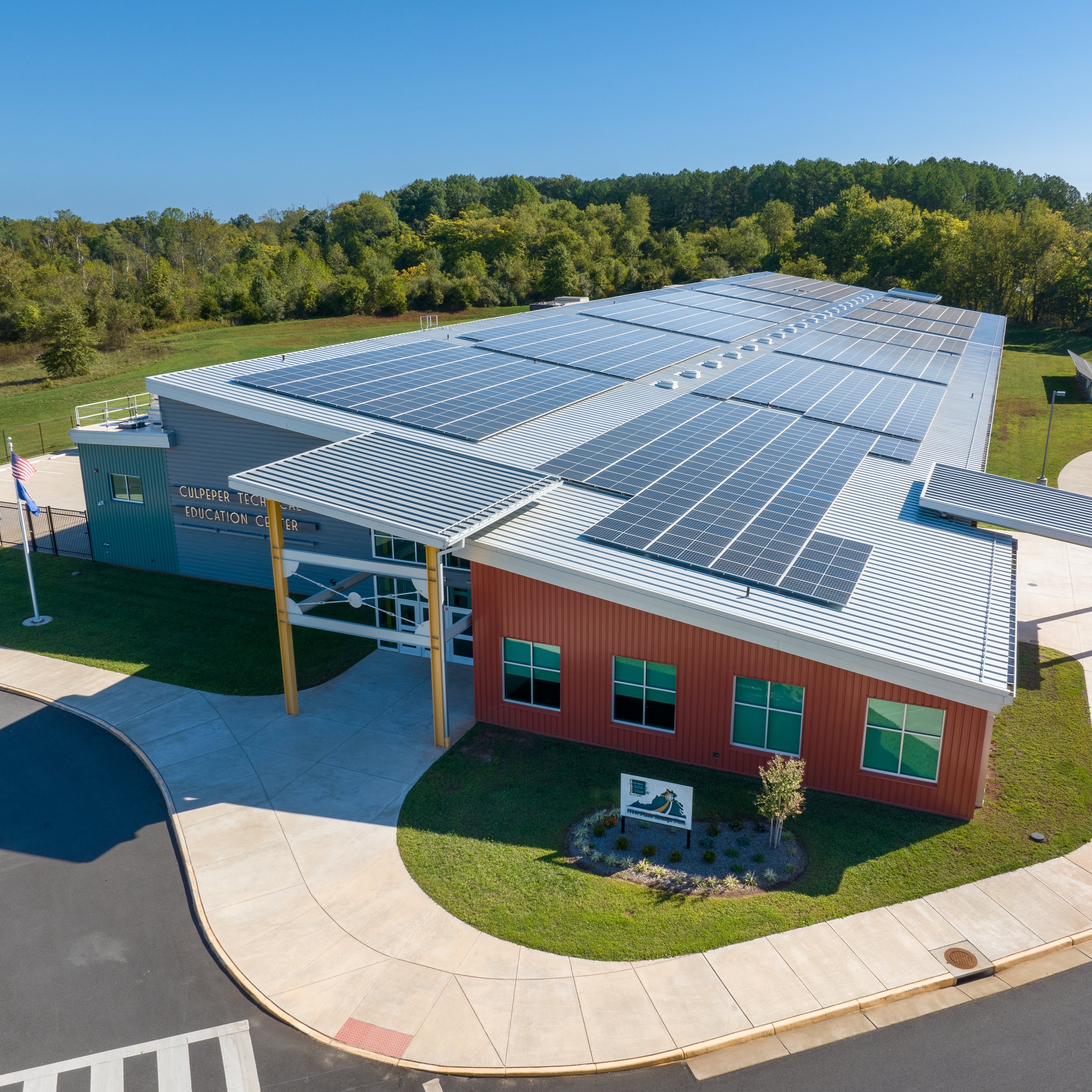 Solar panels on a building's roof, a paved driveway, and greenery in the background.