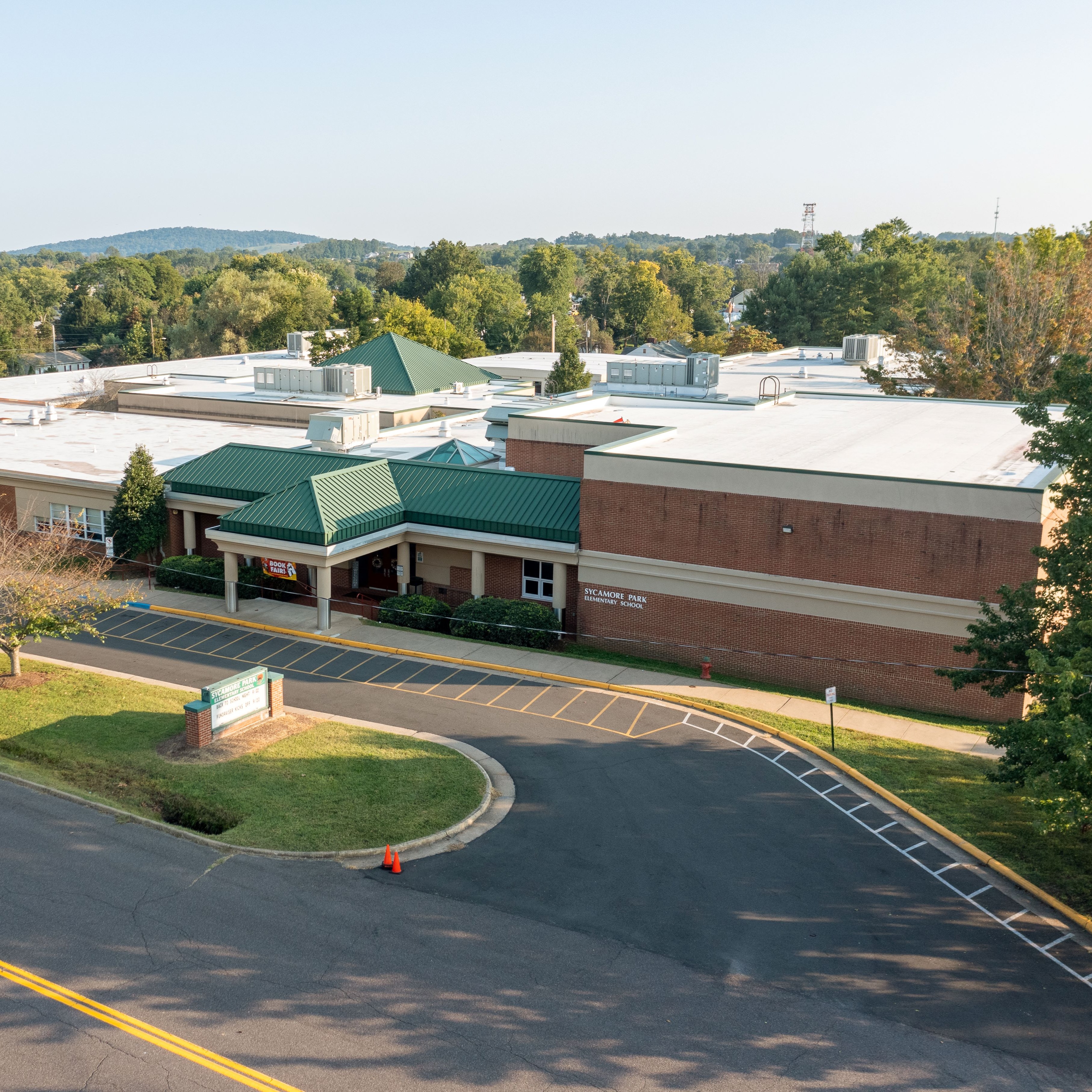 An aerial view of a large building with a green roof. Trees and a parking lot are visible.