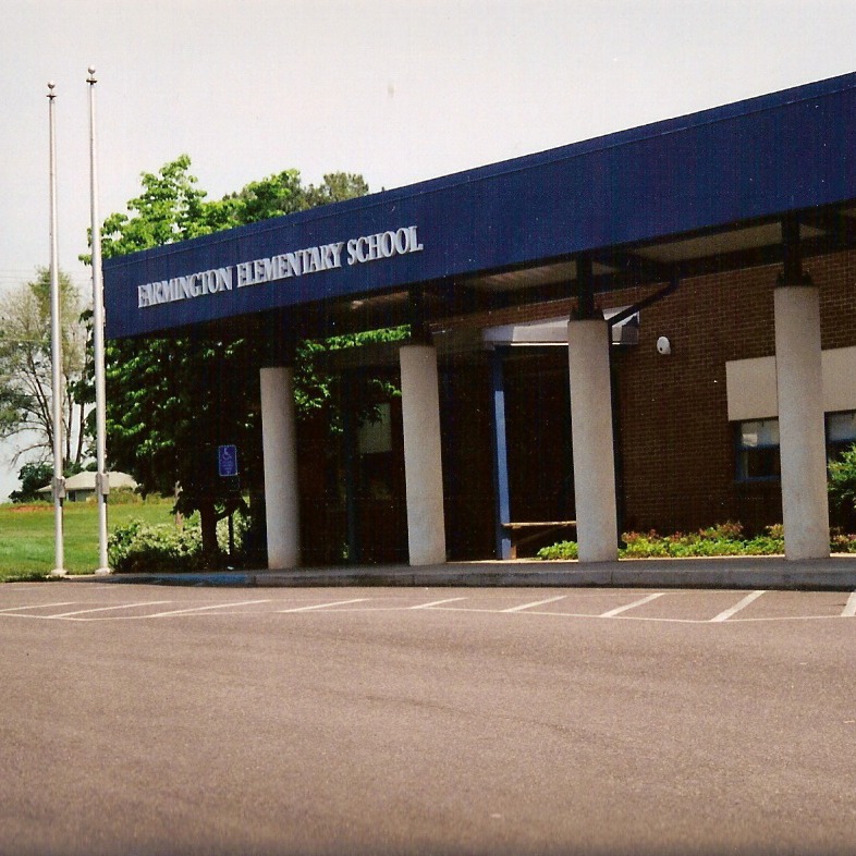 A school entrance with a blue roof, white pillars, and a large parking lot in front.