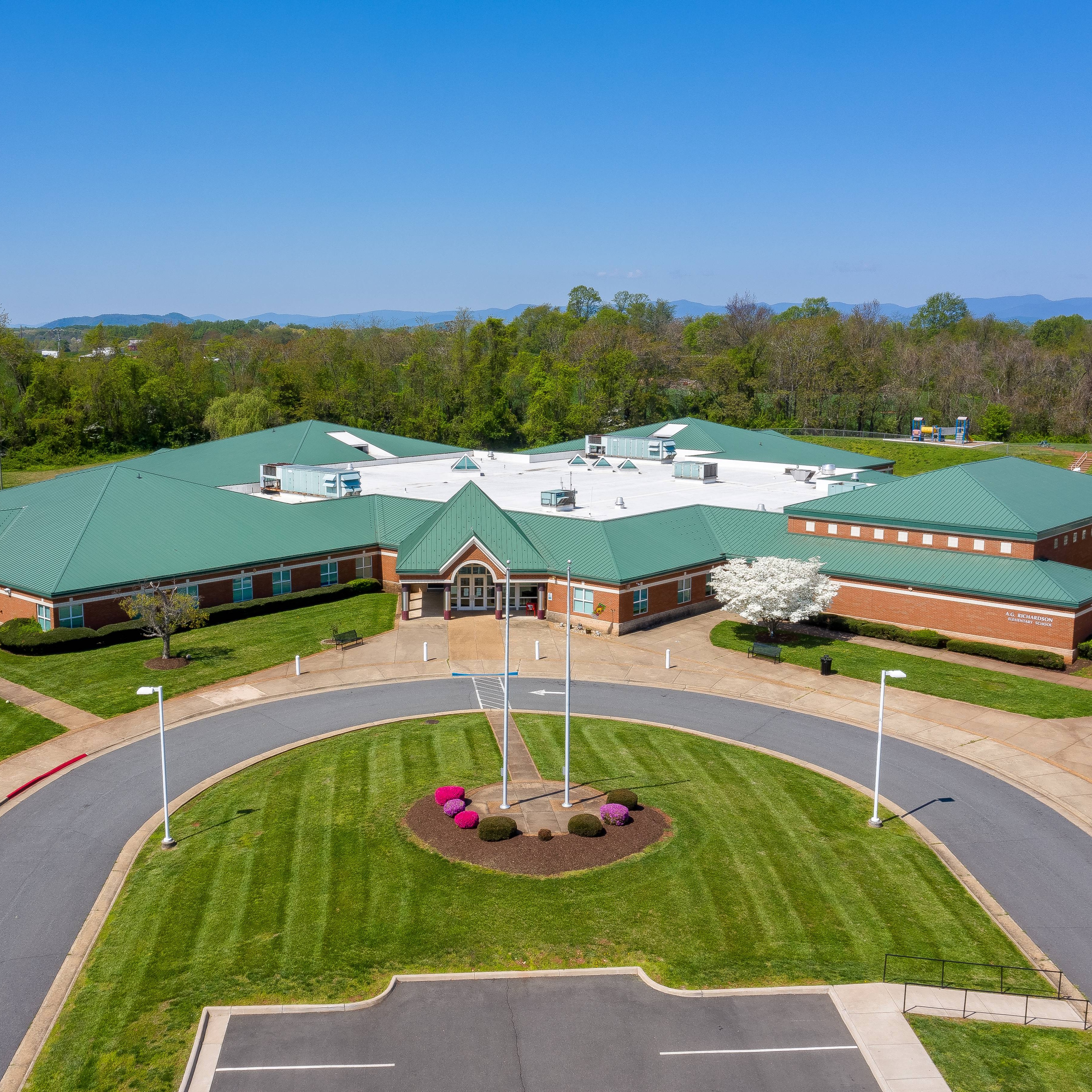 Aerial view of a large building with a green roof, set on a green lawn with trees and shrubs.