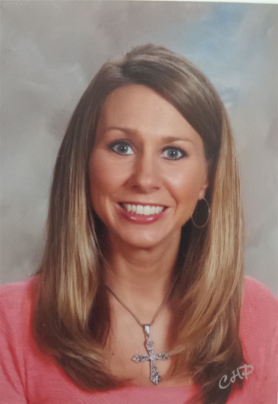 Smiling woman wearing cross necklace and salmon shirt in front of a gray background