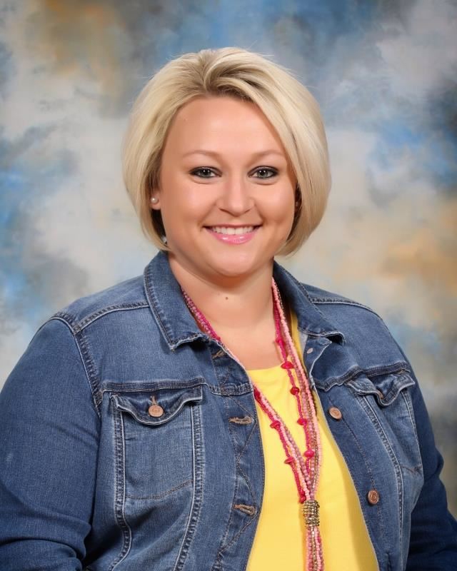 Smiling woman wearing denim jacket over yellow blouse with red necklace in front of blue sky background