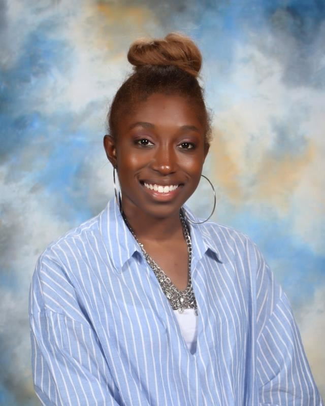 Smiling woman wearing hoop earrings and striped blue blouse in front of bluesky background