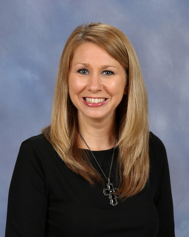 Smiling woman wearing cross necklace and salmon shirt in front of a gray background