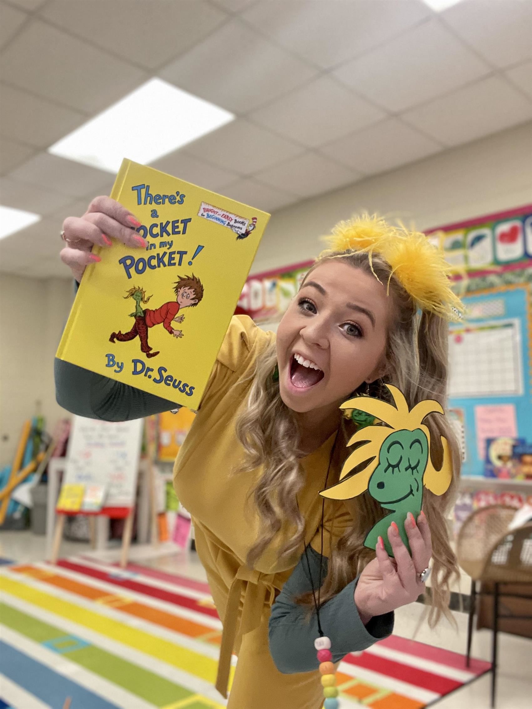 Smiling woman holding There's a Wocket in your Pocket by Dr. Seuss book while dressed as a yellow Seuss character