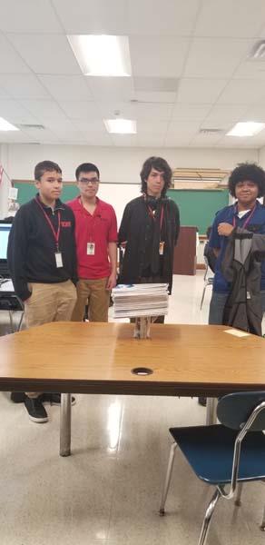 Four male students standing together in a classroom.