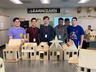 A group of 6 students standing next to the home models they built.