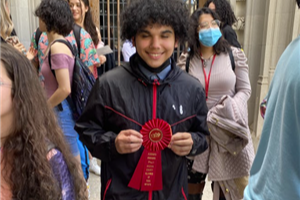 photo of Noah Perez posing with his red ribbon; wearing a black jacket and denim jeans