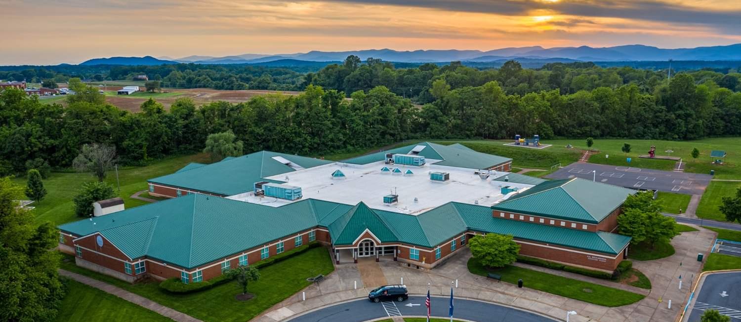 Aerial view of a school building with green roofs, surrounded by green grass, trees, and a circular drive.