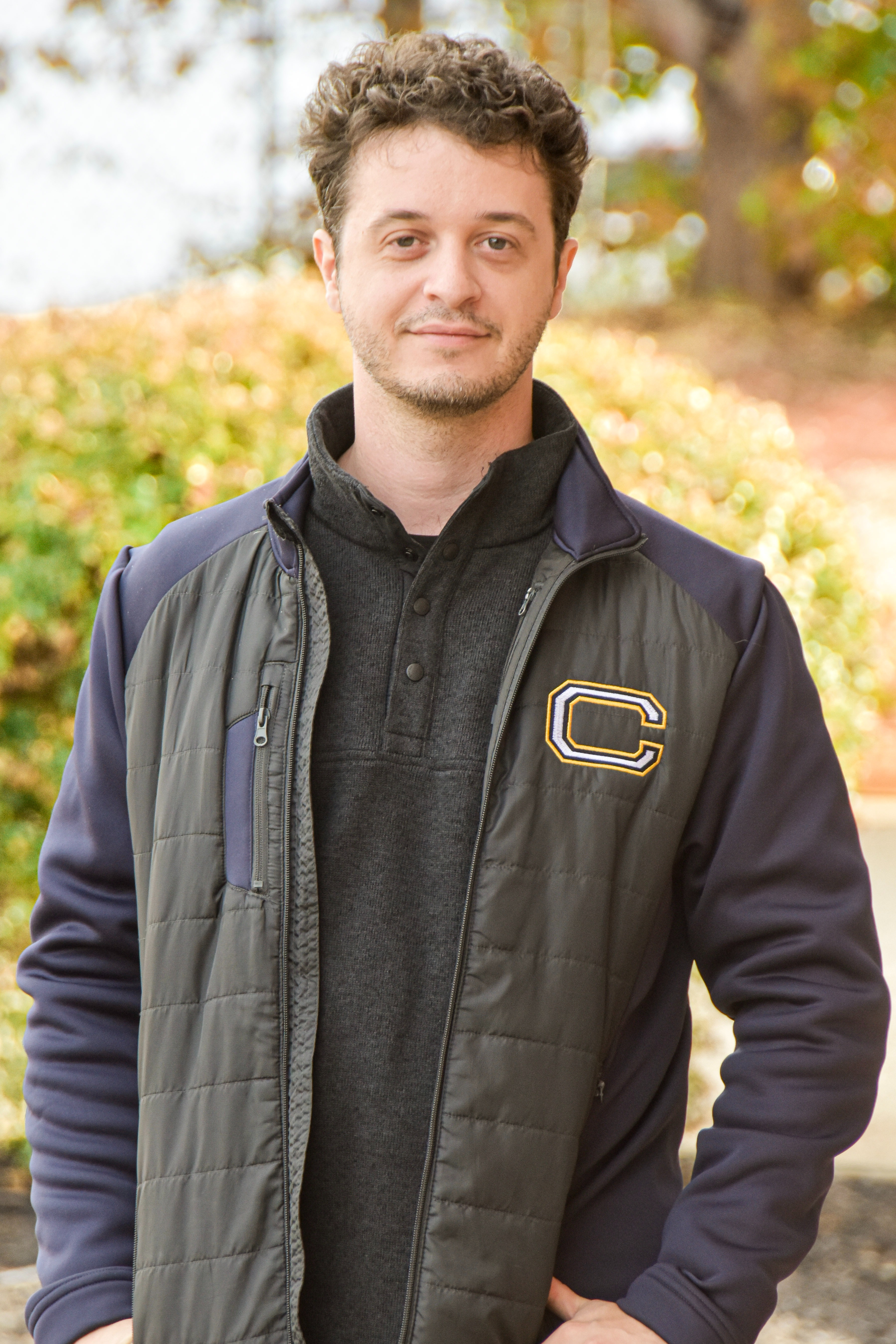 A man stands outside with a jacket featuring the letter "C" on the front, smiling.