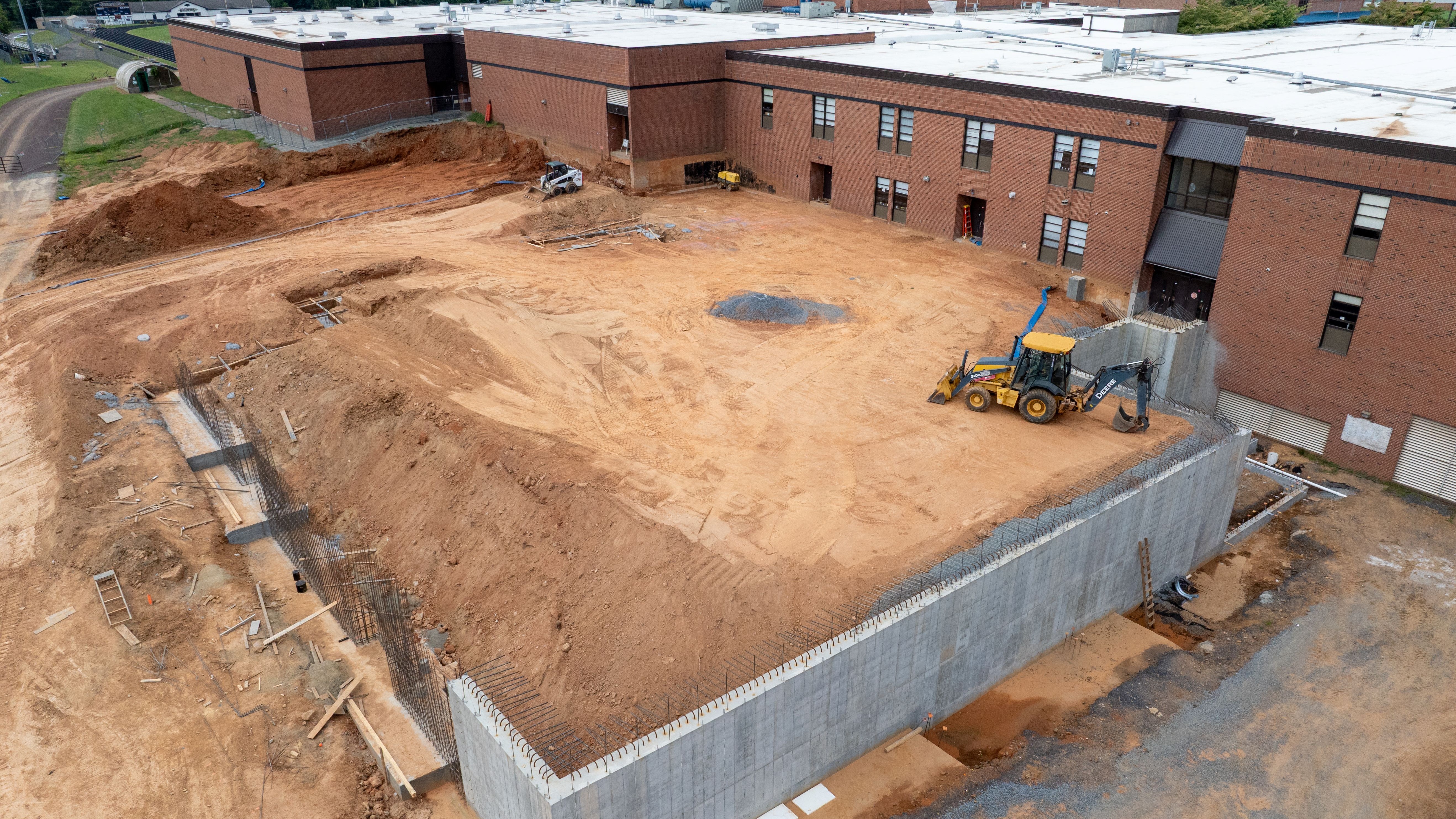 view of contruction site behind a school building with a large dirt pile contained by a block wall