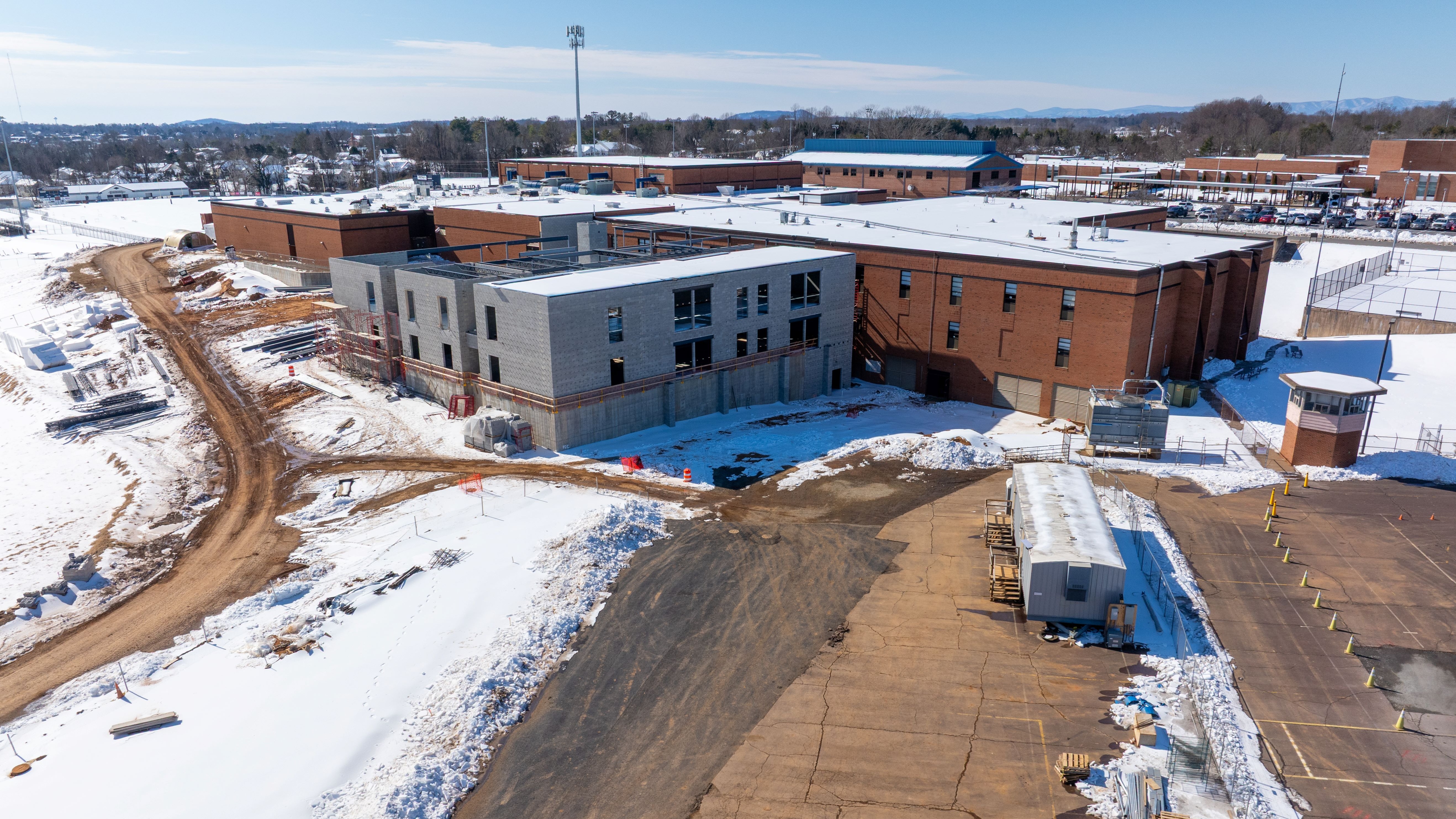 photo of a school with a construction renovation on the back with snow on the ground all around and on the roof of the existing building