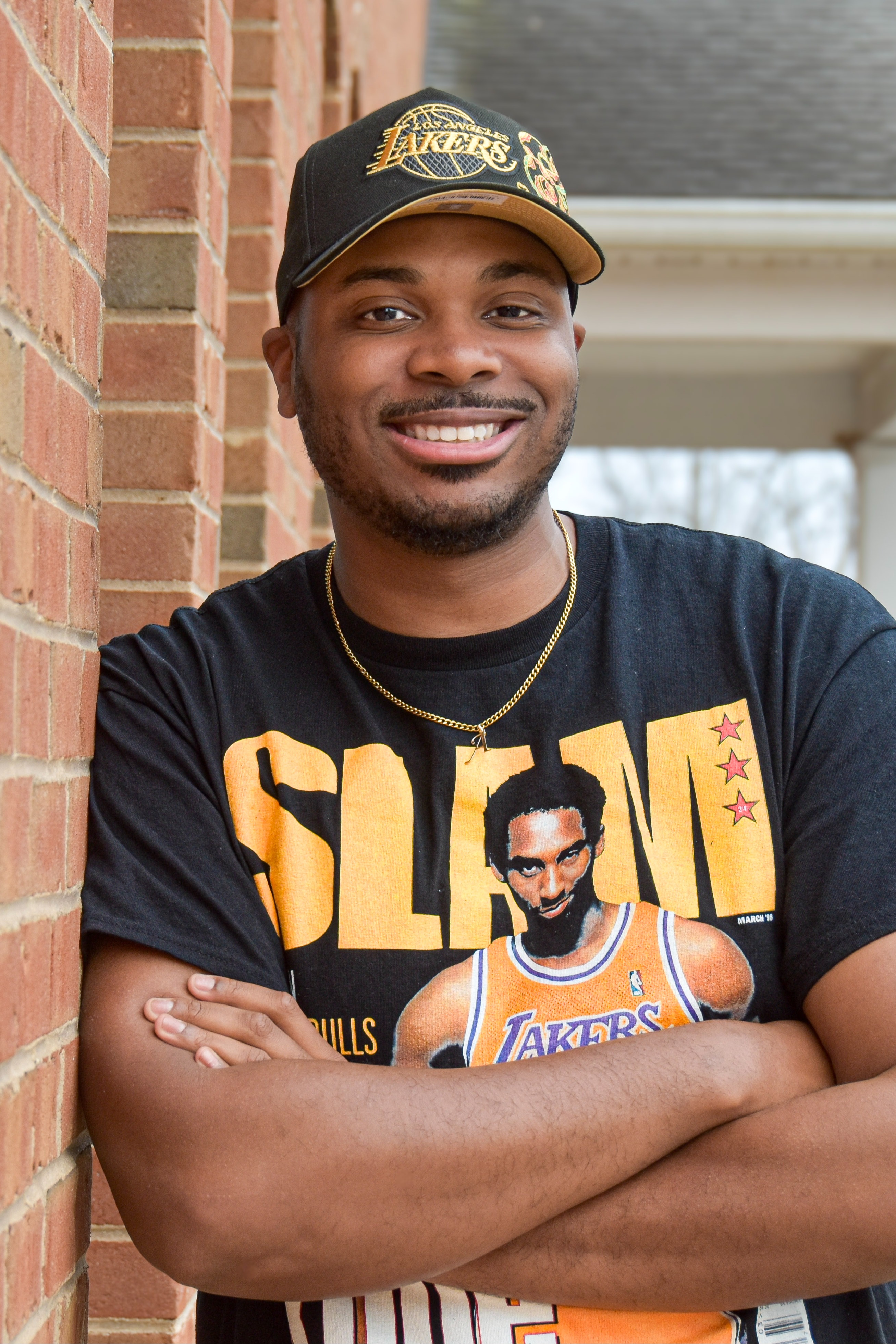 Man leaning against a red brick wall wearing a Lakers shirt with a player on it.
