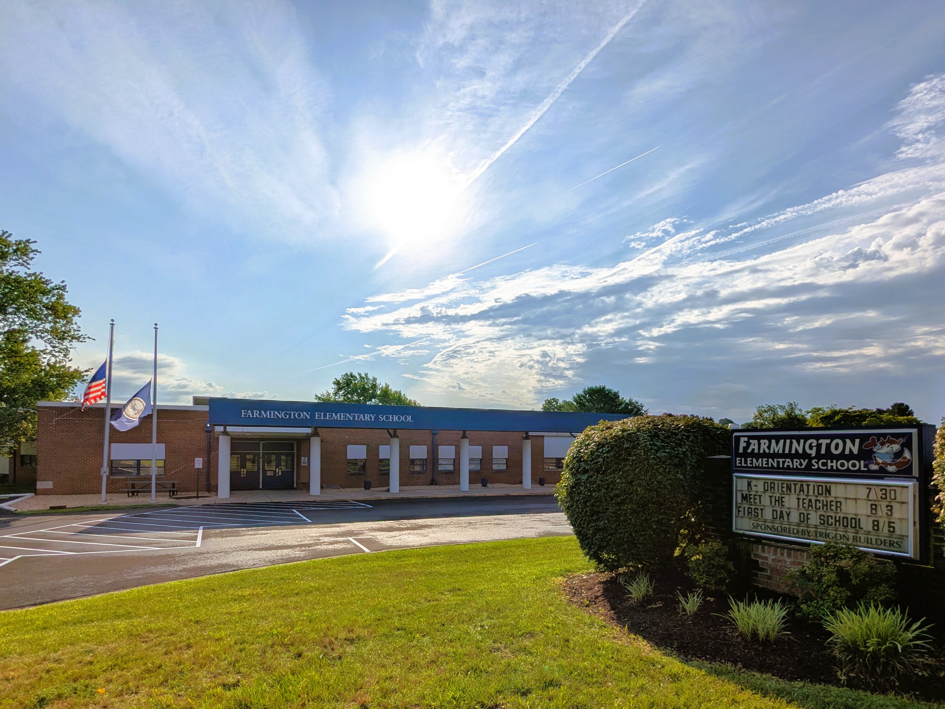Bright blue sky above a school building with a sign reading "FARMINGTON ELEMENTARY SCHOOL". Two flags on poles behind the building.