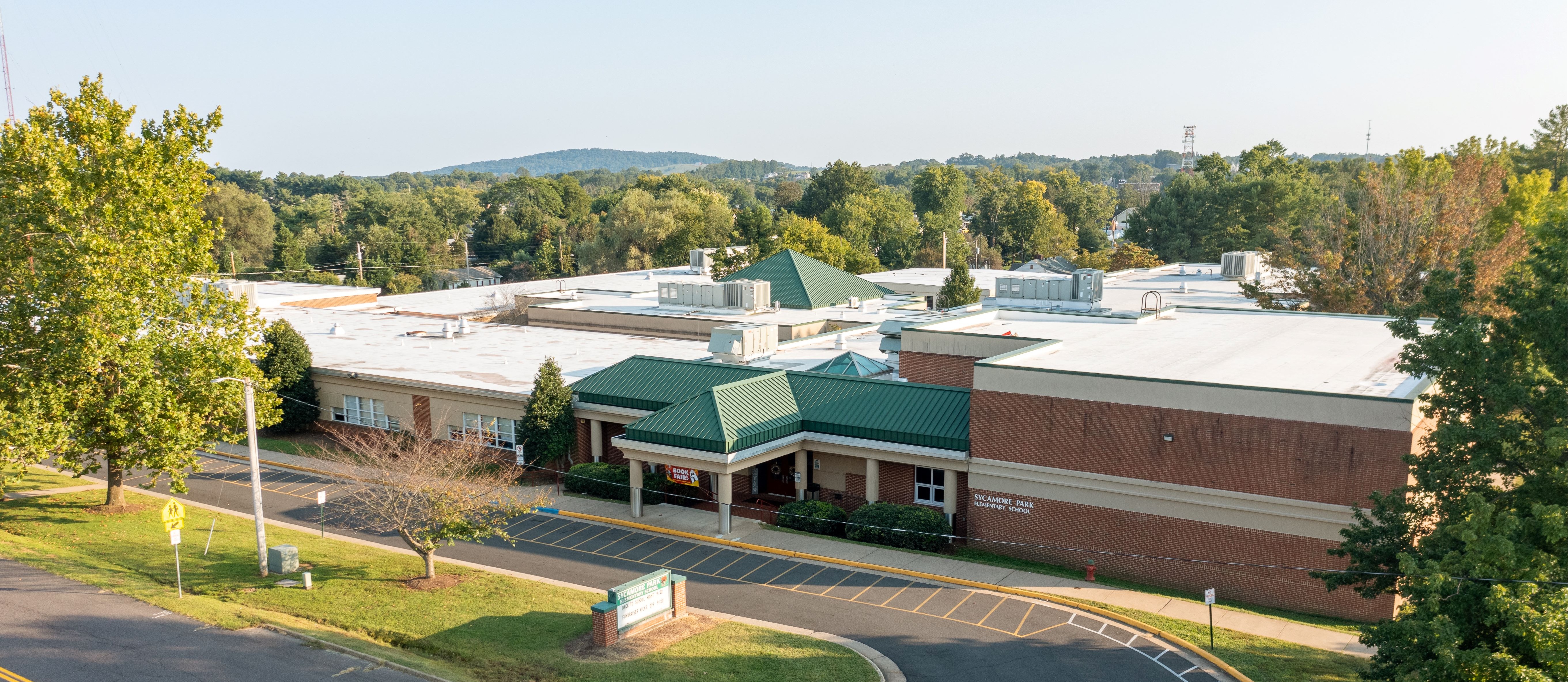 Aerial view of a large building with green roof. Trees and a parking lot surround the building.