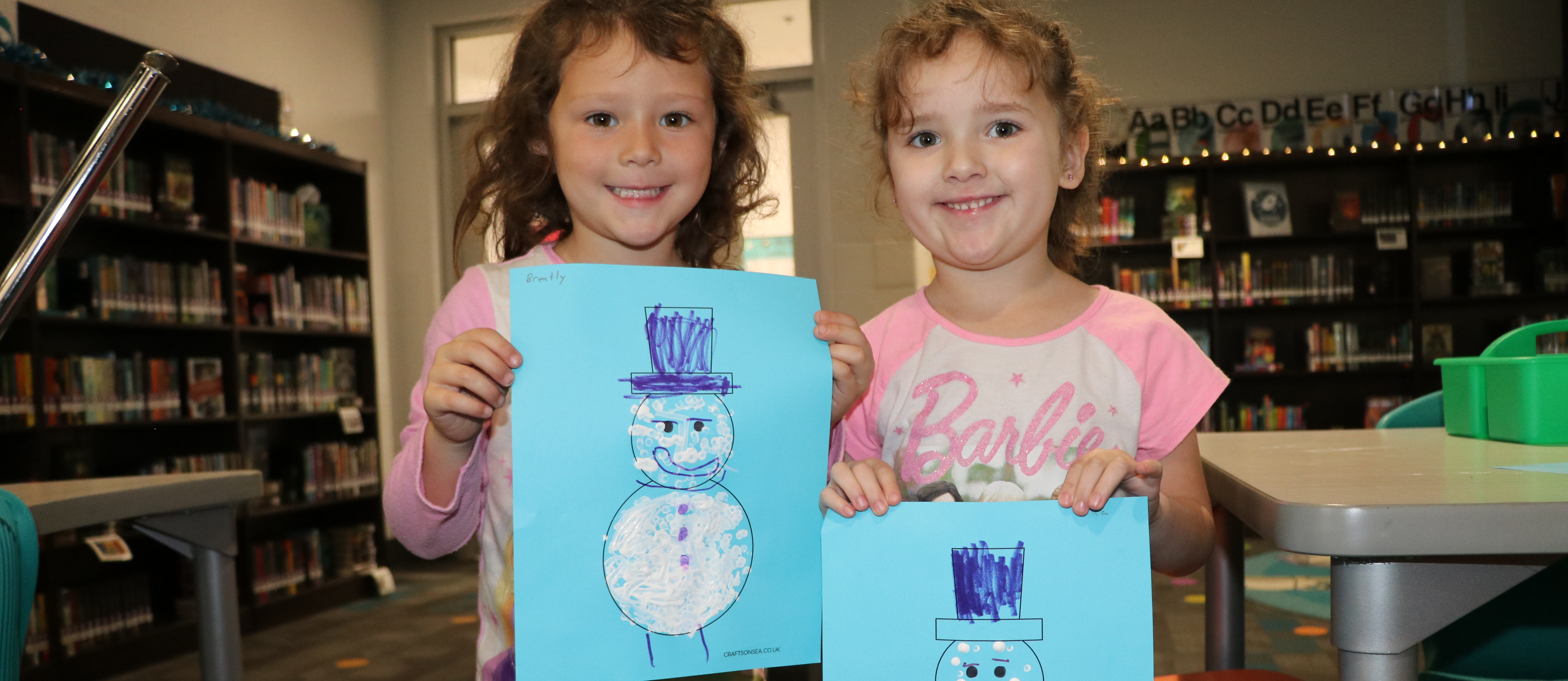 Girls show the snowmen they made in library