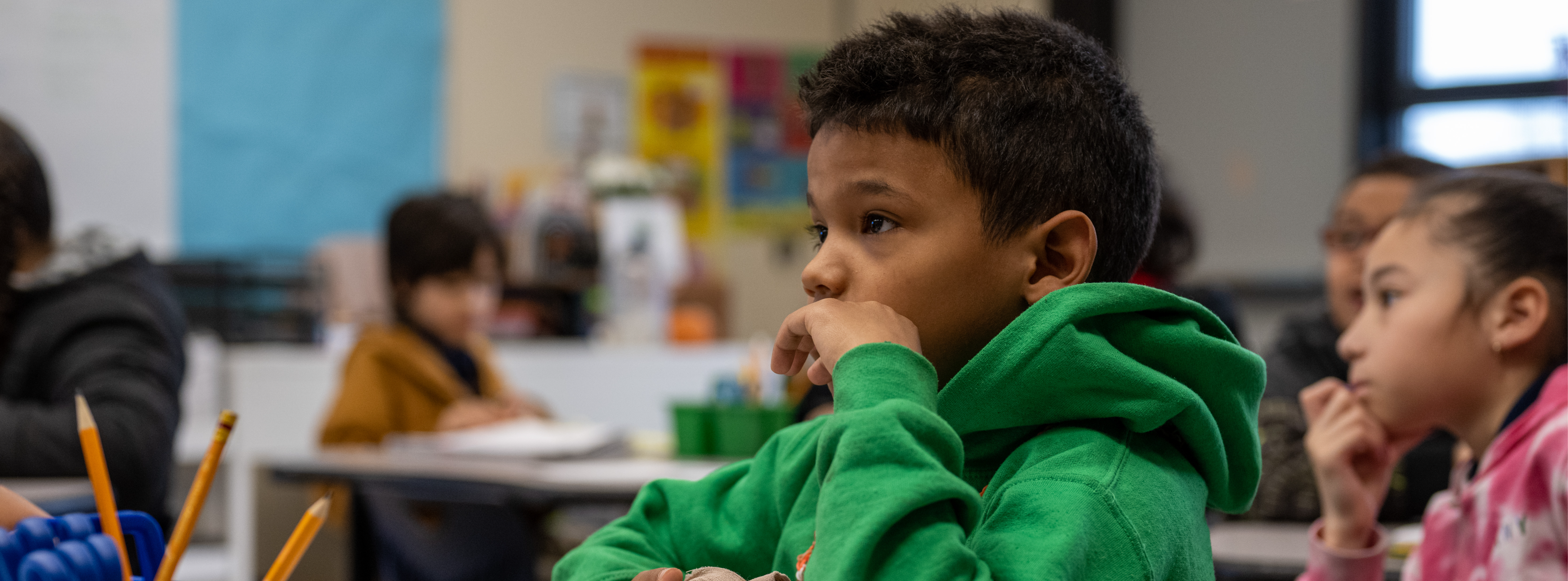 Kelly student in green sweater focused in class with classmates in the background. 