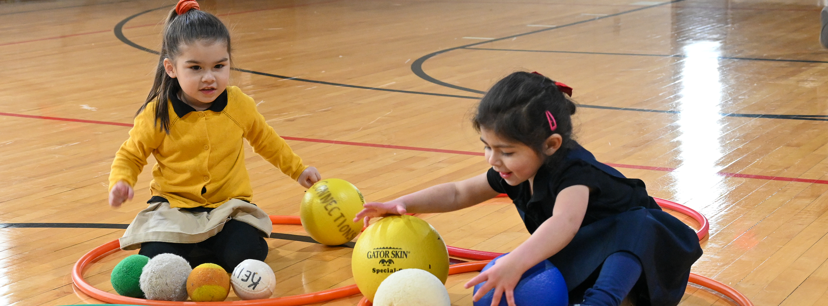 Two young students play with balls and hula hoops