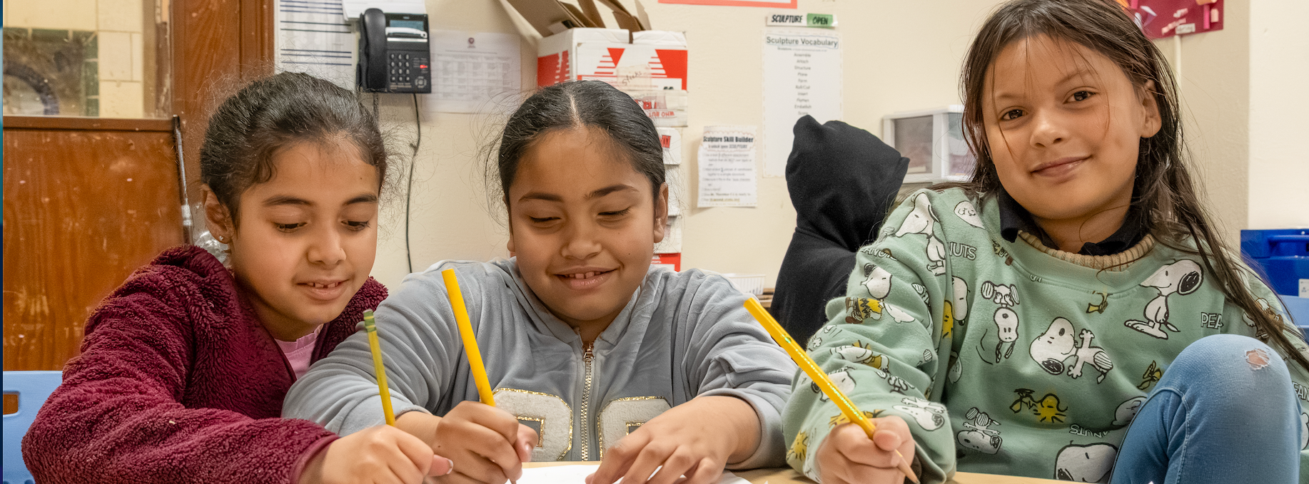 Three students write their assignments while giggling