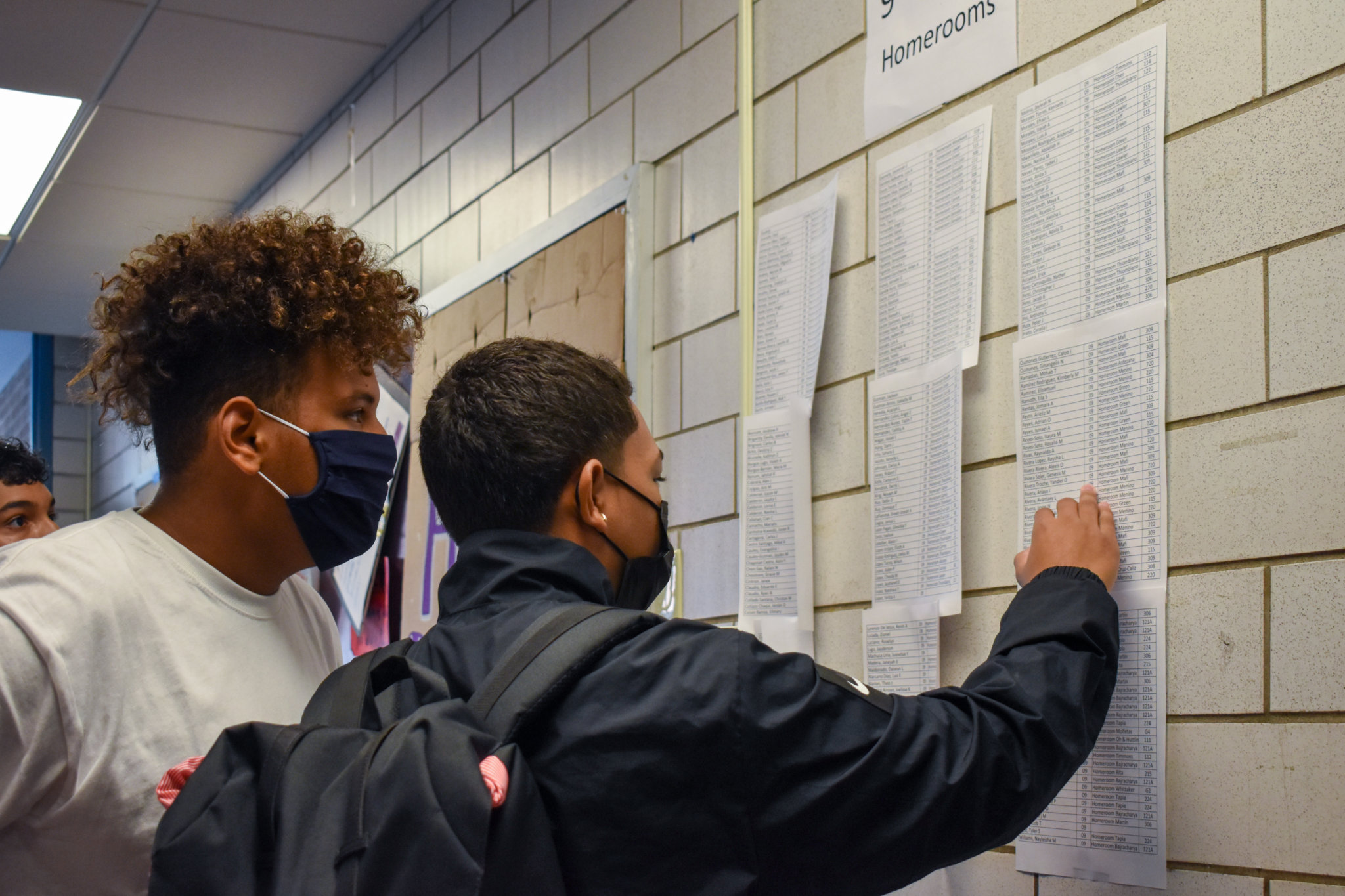 2 students looking at sheets of paper taped on the wall in the hallway