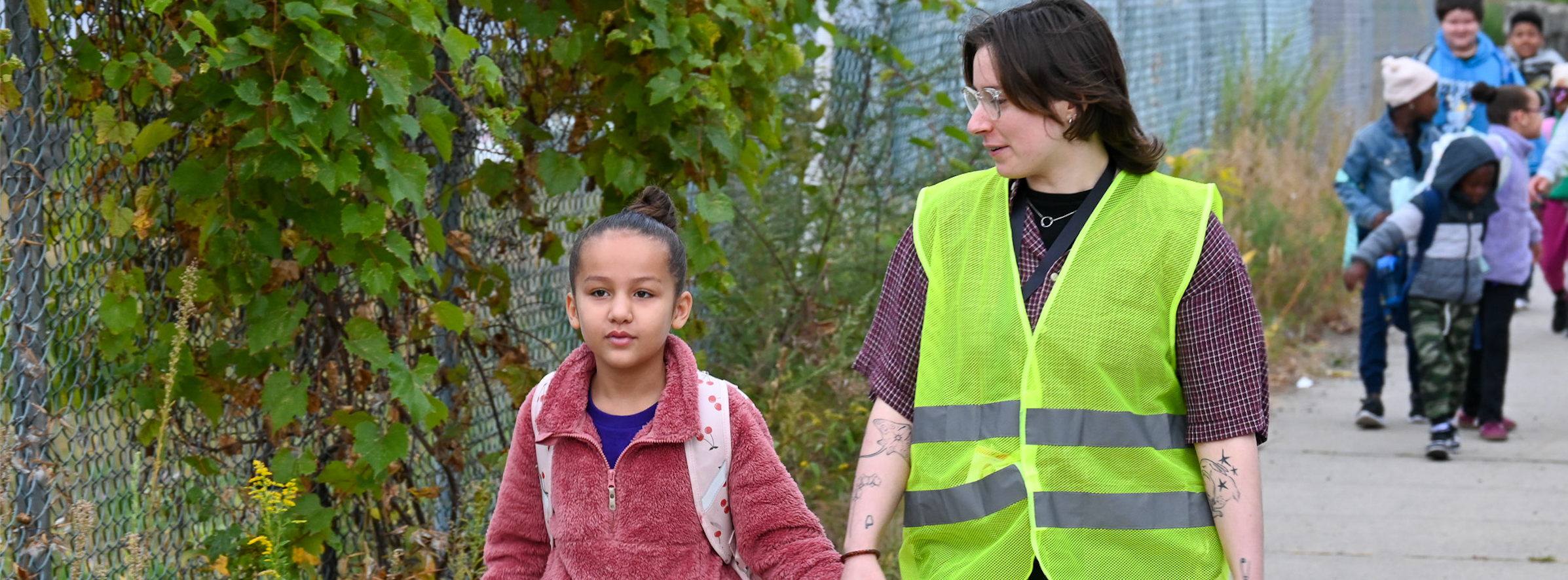 A teacher and student hold hands walking to school
