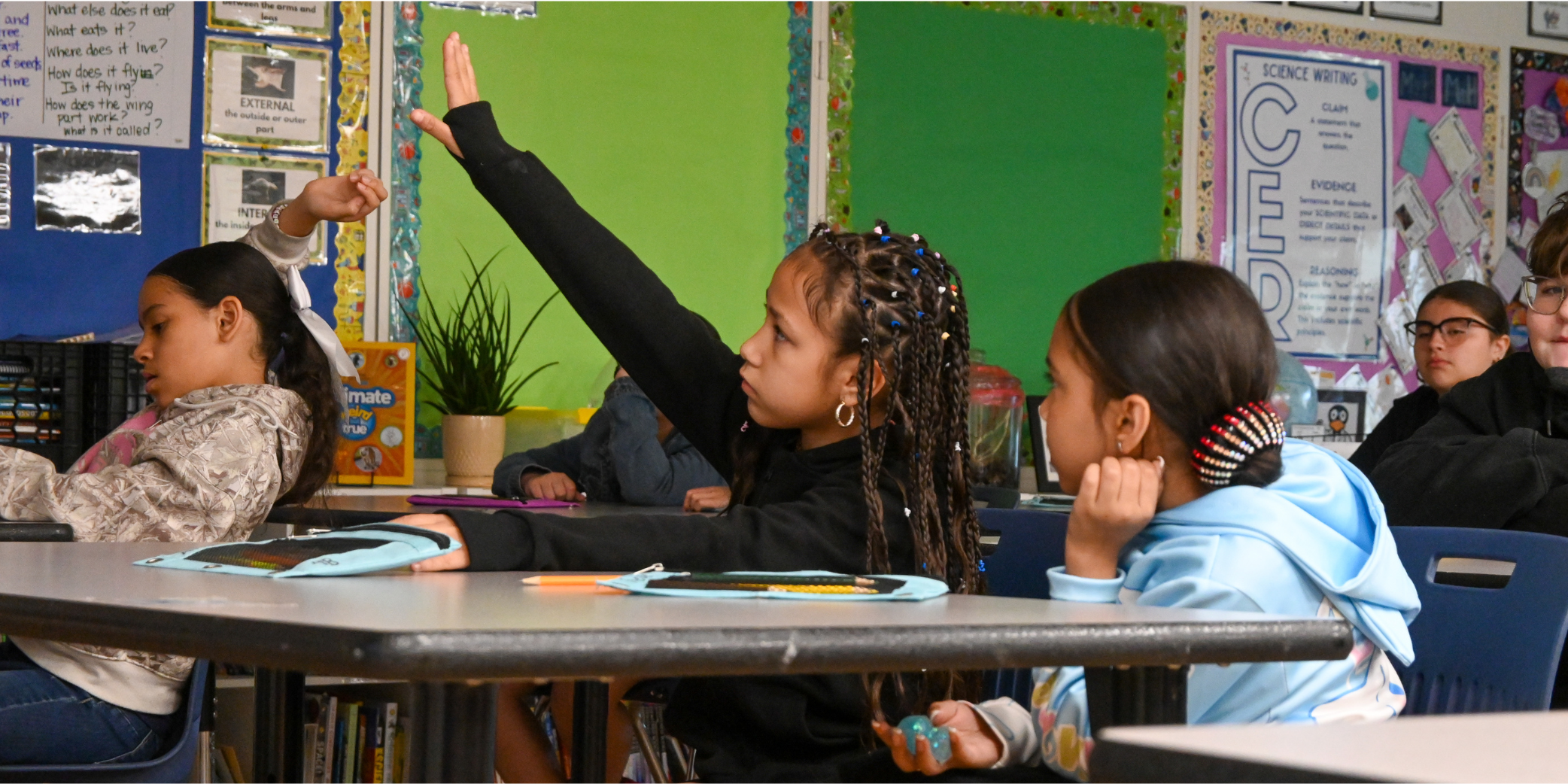 student sitting at table raising hand in class