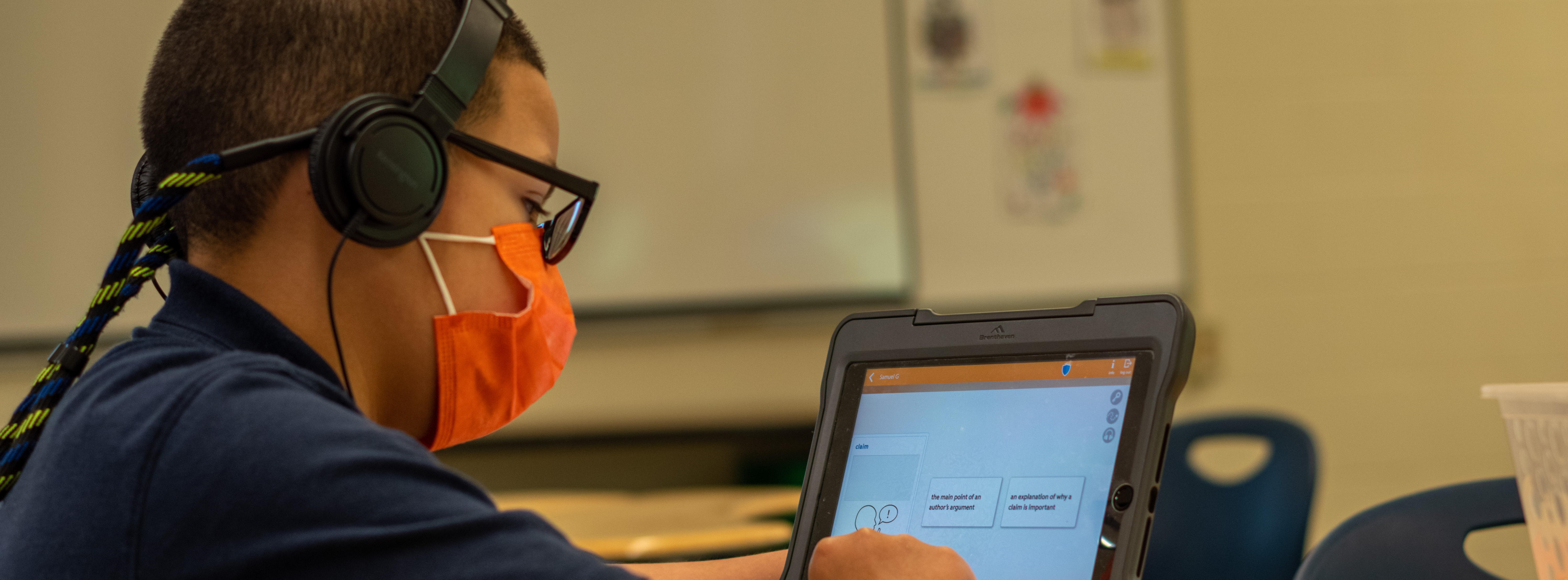 Student working on his iPad with an orange face mask on 
