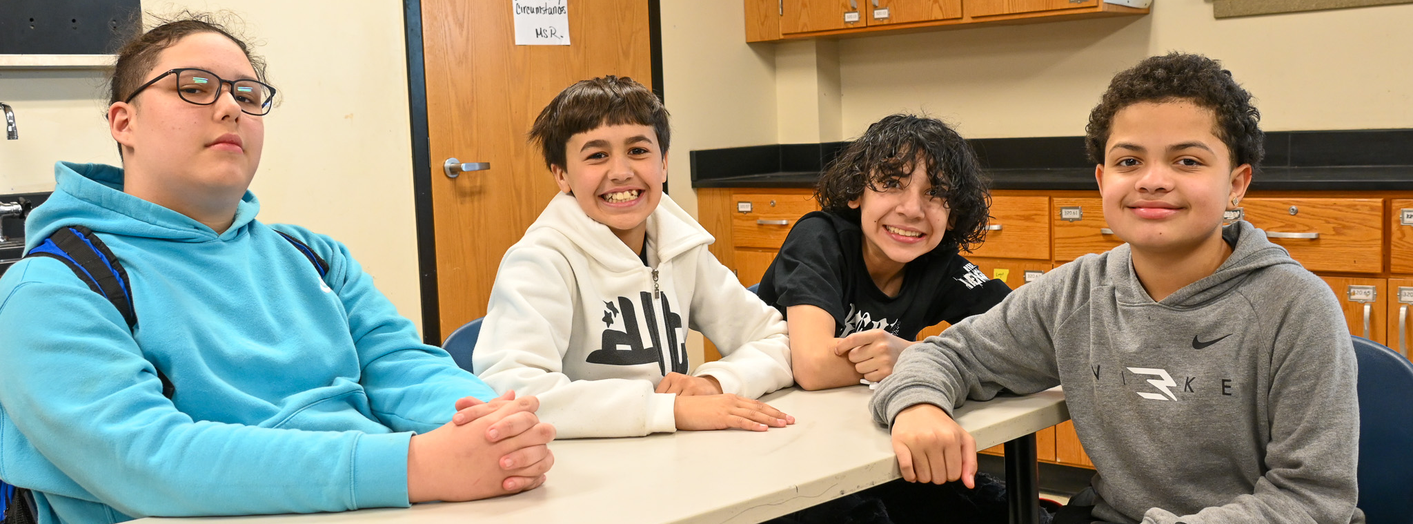Four students smile at the camera in class