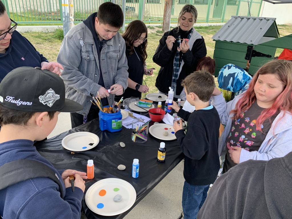 students stand around a picnic table as they help paint the free little library