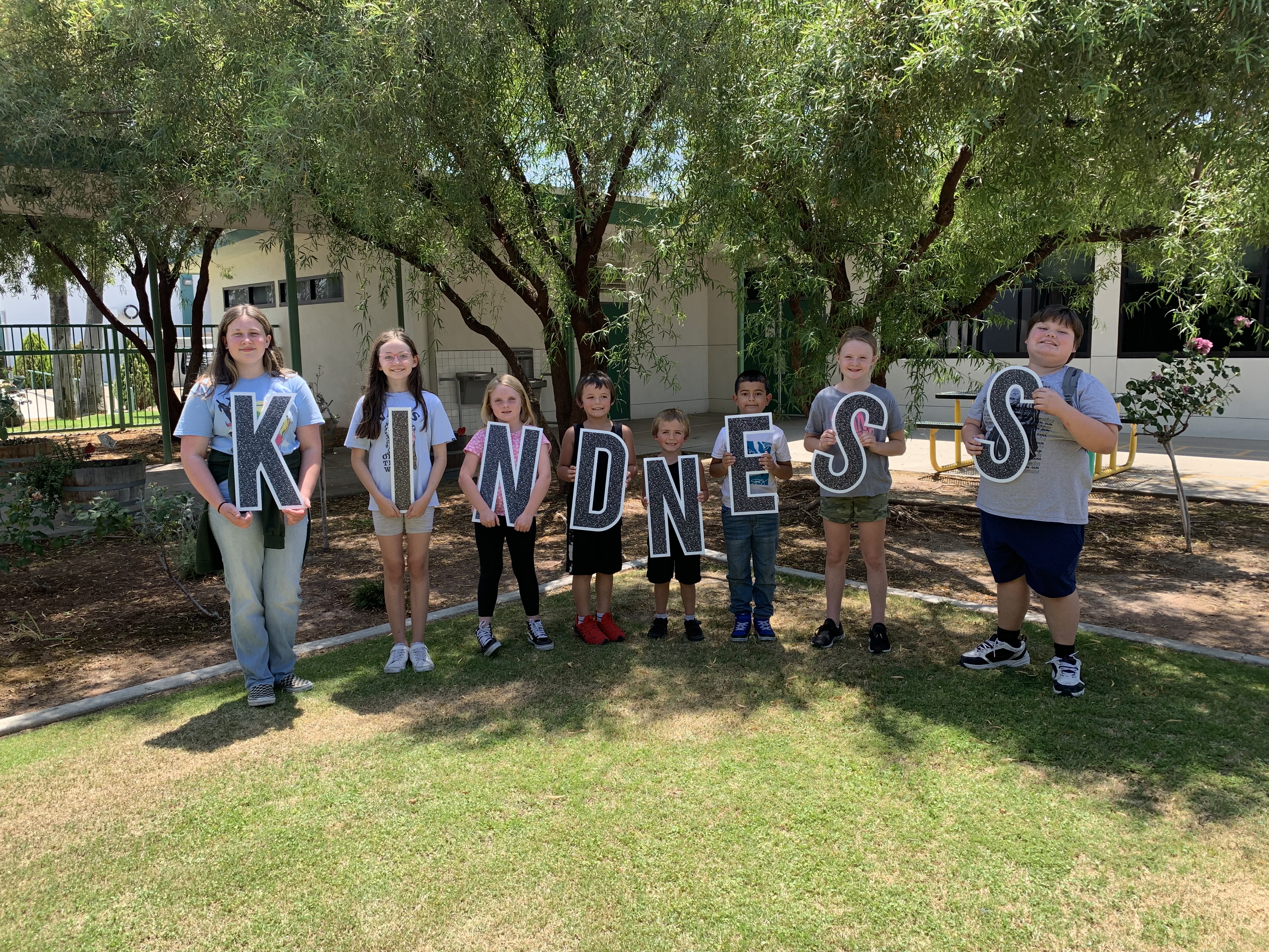 Students standing in front of garden holding letters that spell out the word kindness